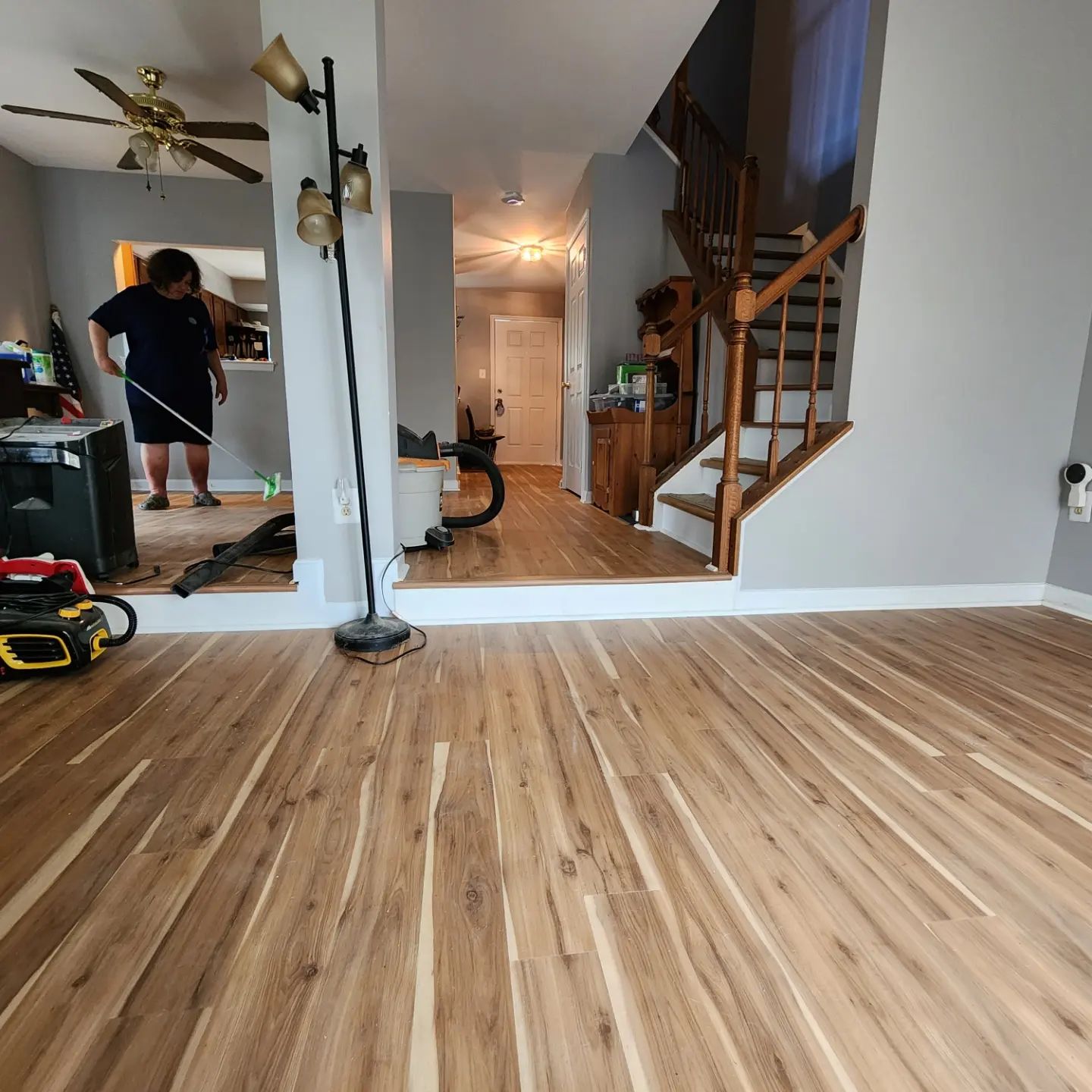 Living room with wood floors, staircase, and a wall mirror reflecting a person in a black shirt and shorts.