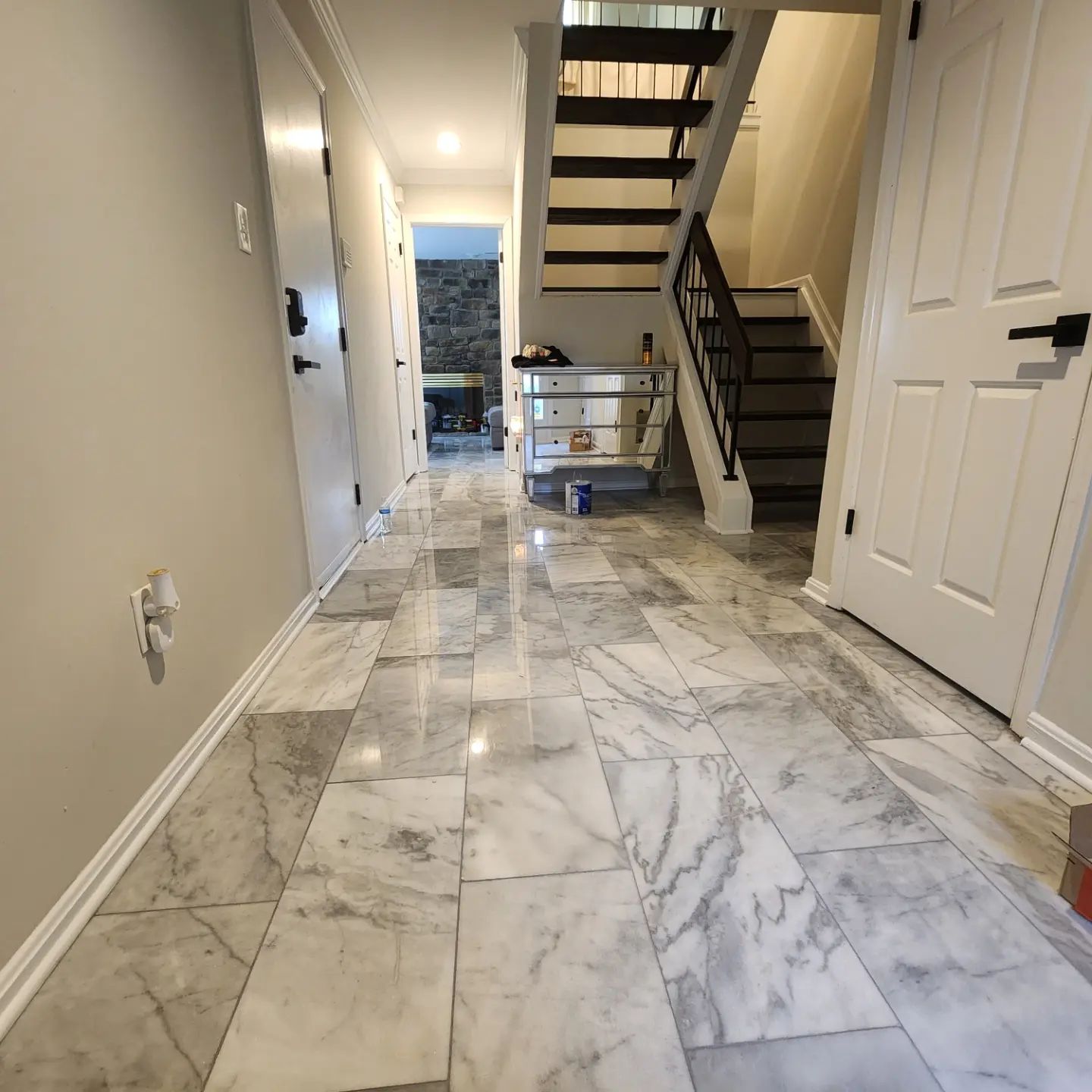 Marble-floored hallway with staircase, white doors, and moving supplies under warm indoor lighting