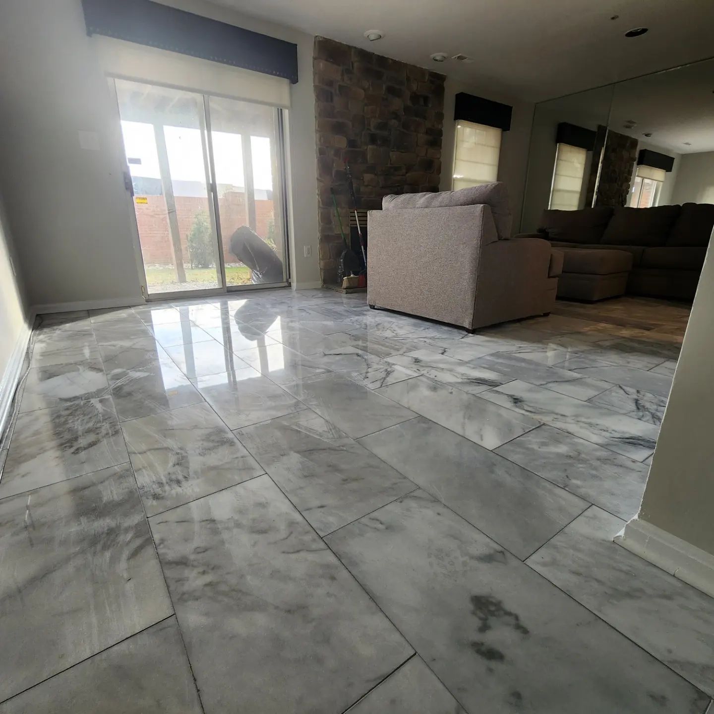 Bright marble-tile living room with large windows, stone fireplace, and beige sofas.