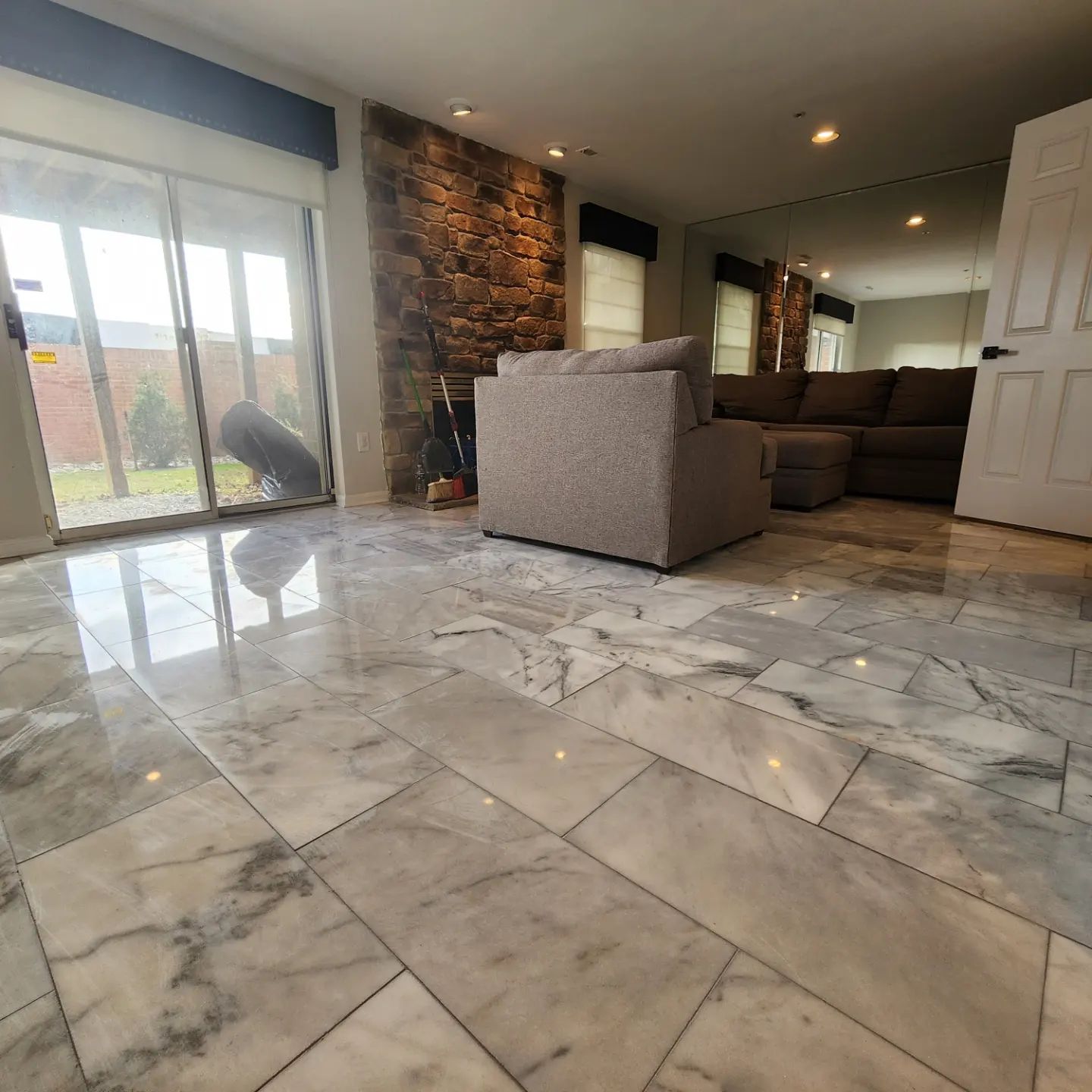 Modern living room with glossy marble floor, gray sofa, stone accent wall, and sliding glass doors