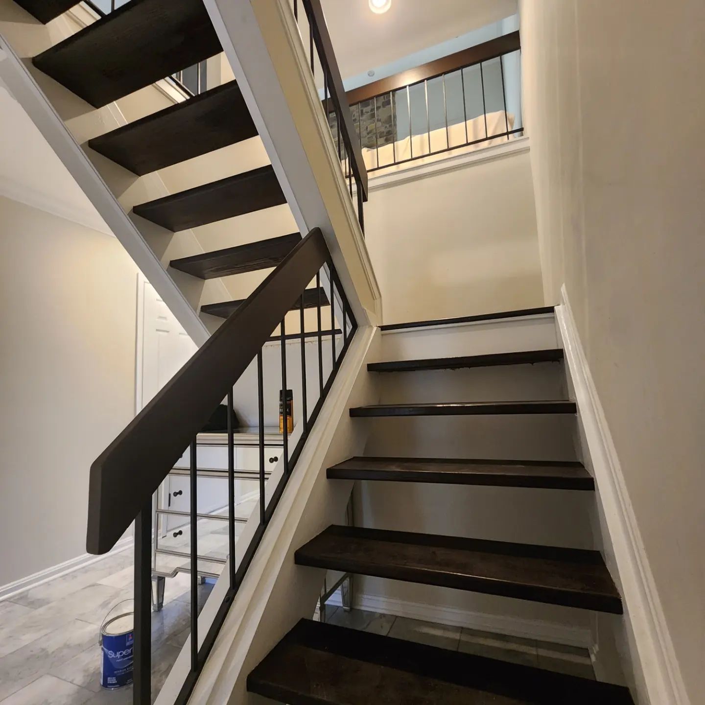 Stairwell with dark wooden steps, white walls, and black railings in a narrow interior space