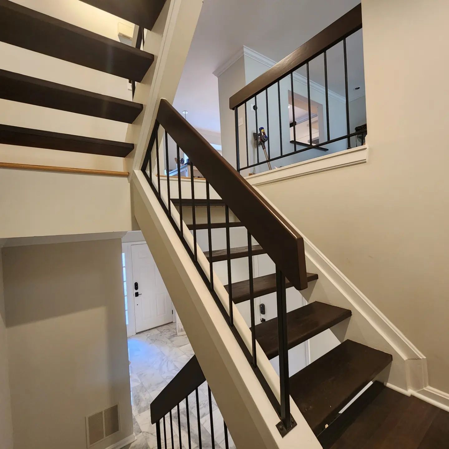 Interior staircase with dark wood steps, black railing, and beige walls in a bright home.