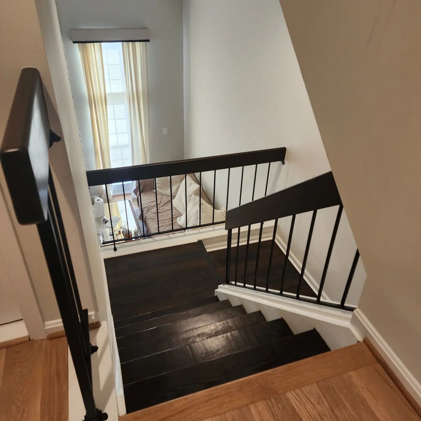 Staircase with dark wood steps, white walls, black railings, and a window at the landing.