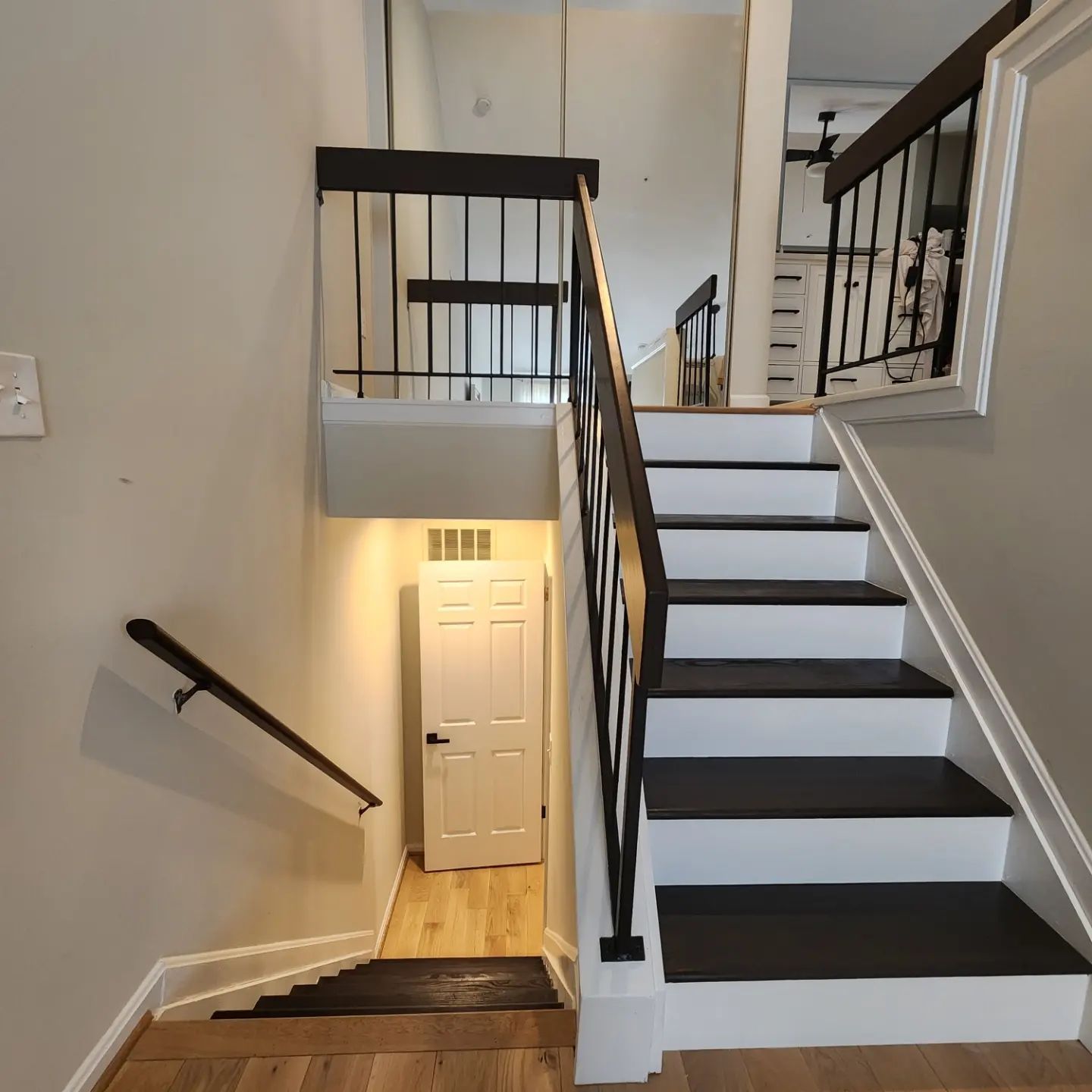 Indoor staircase with black-and-white steps, gray walls, and a white door at the landing below.