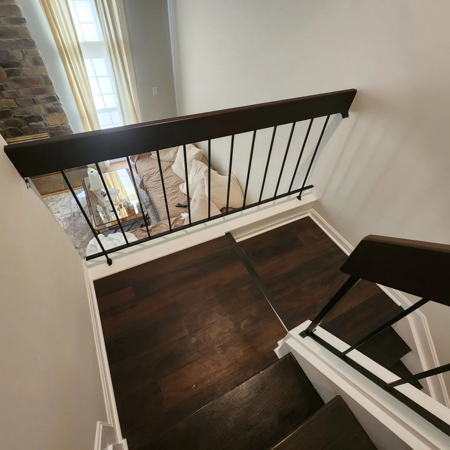 Stairwell landing with dark wood floor, black railing, and stone wall beside a window.