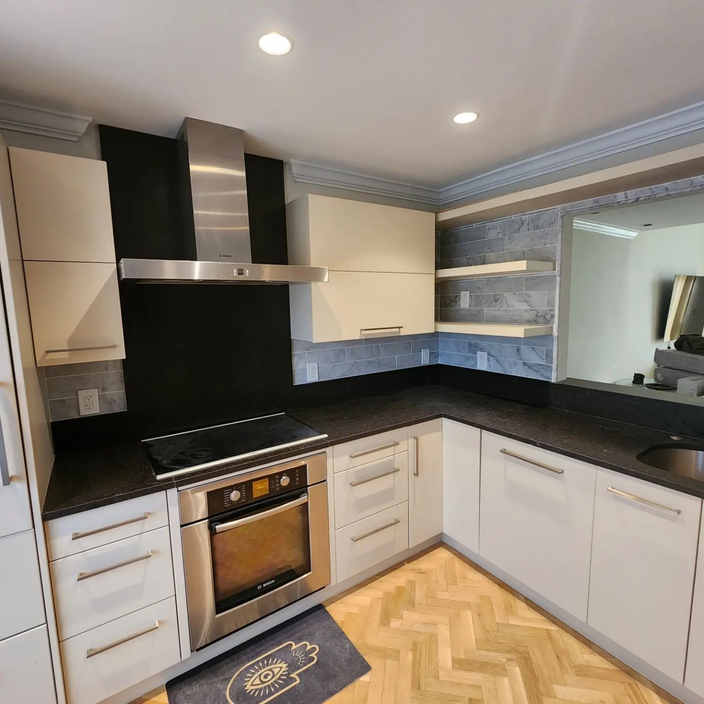 Modern U-shaped kitchen with white cabinets, black countertops, stainless-steel oven, and herringbone wood floor.