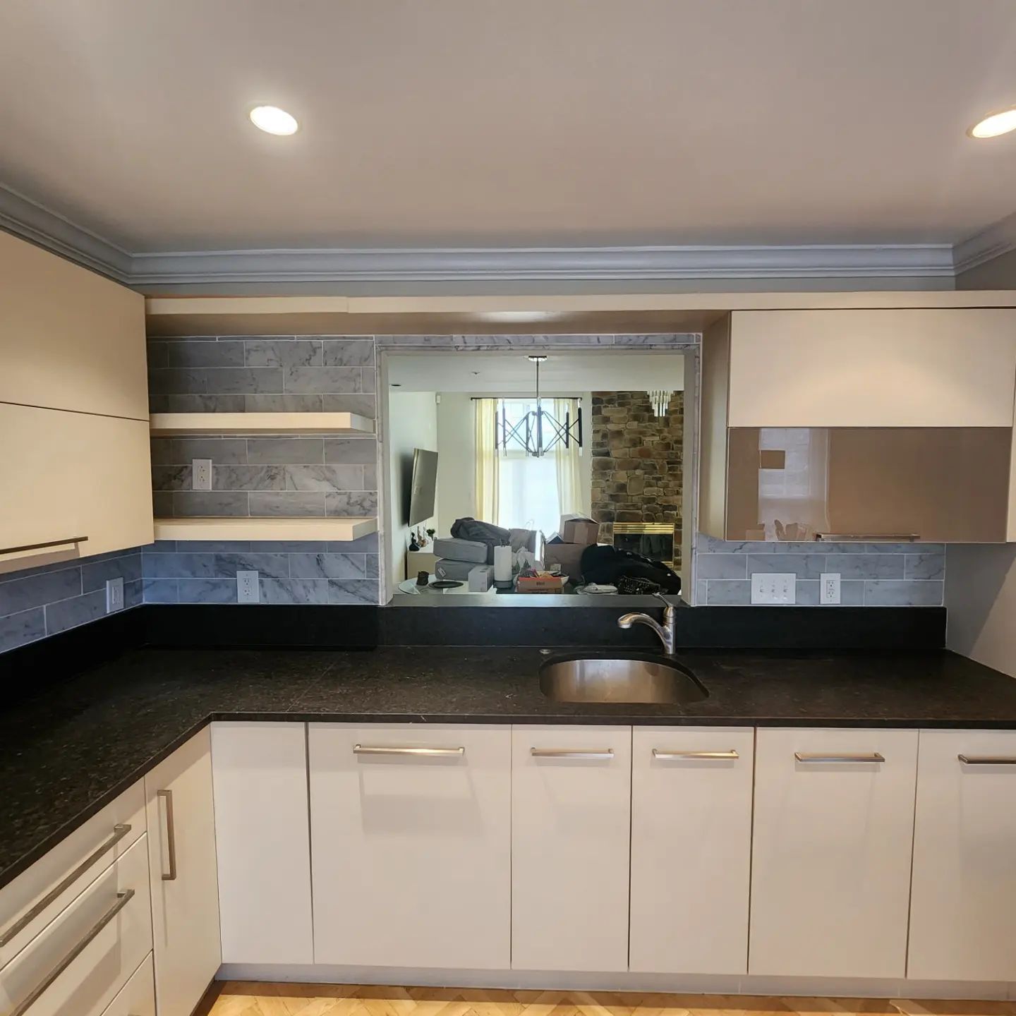 Modern kitchen with black countertops, white cabinets, built-in microwave, and a pass-through opening to another room
