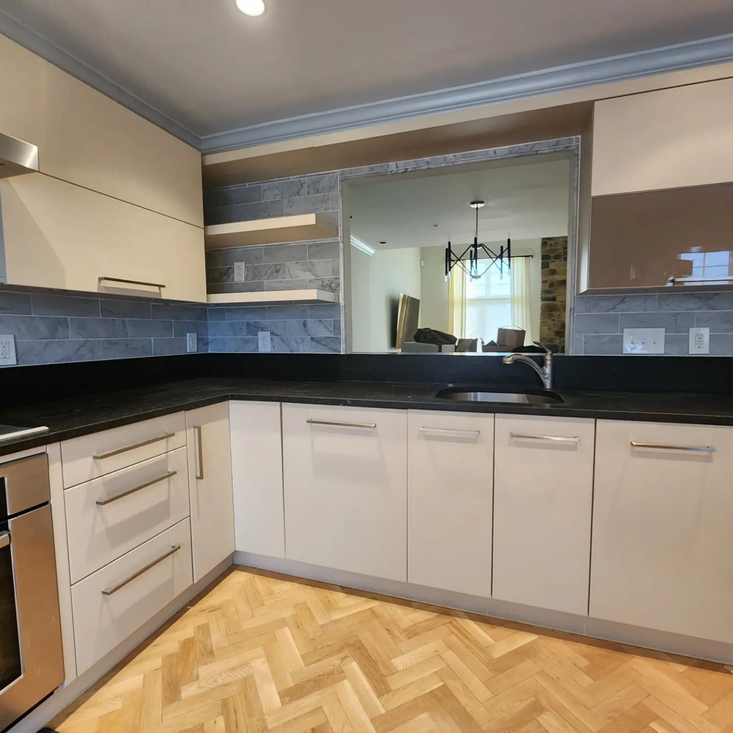 Modern kitchen with beige cabinets, black countertops, blue backsplash, and wood herringbone floor