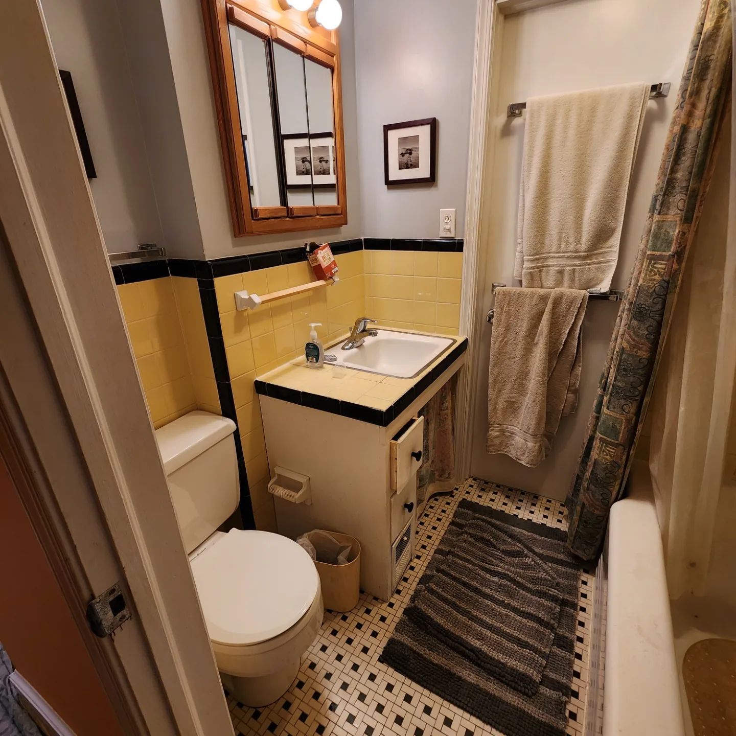 Small bathroom with a toilet, sink, striped rug, yellow walls, mirror, towel rack, and shower curtain.