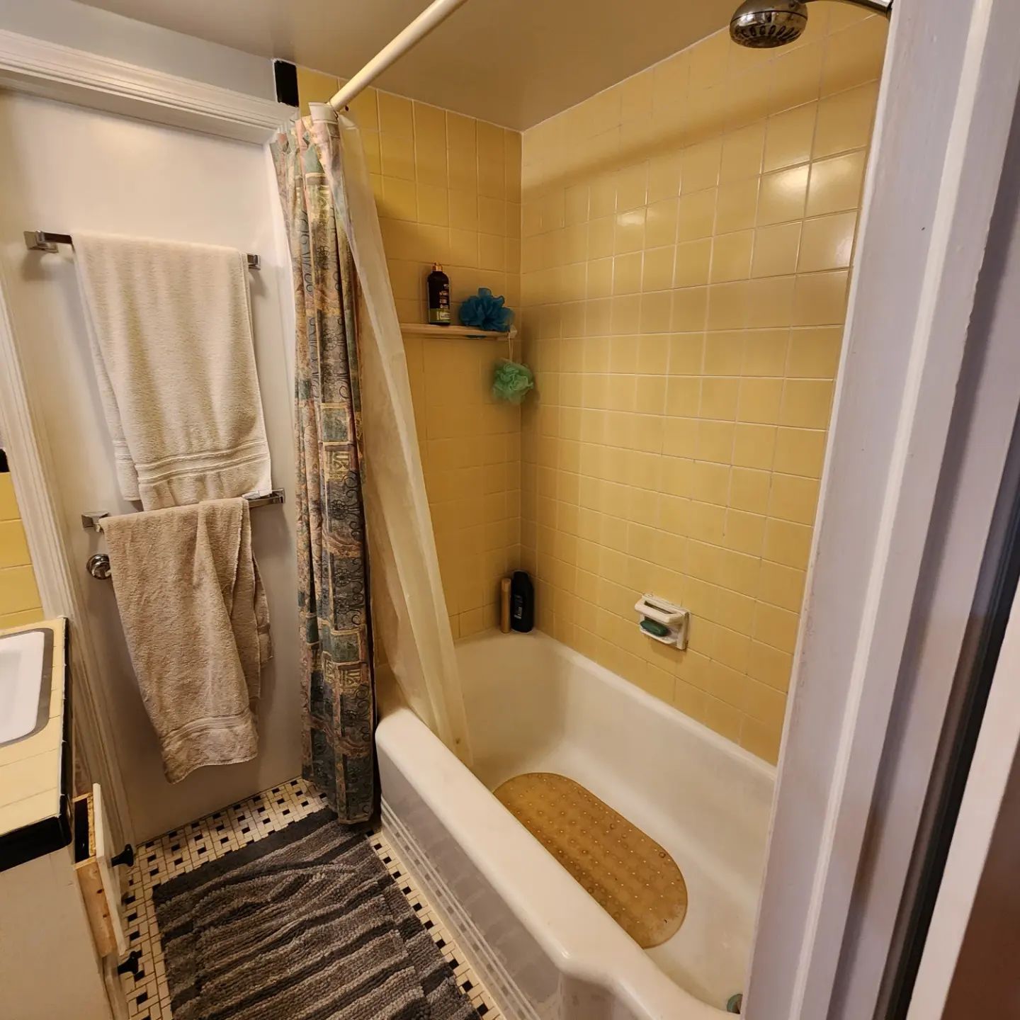 Small bathroom with a bathtub, yellow tile walls, shower curtain, and striped floor mat