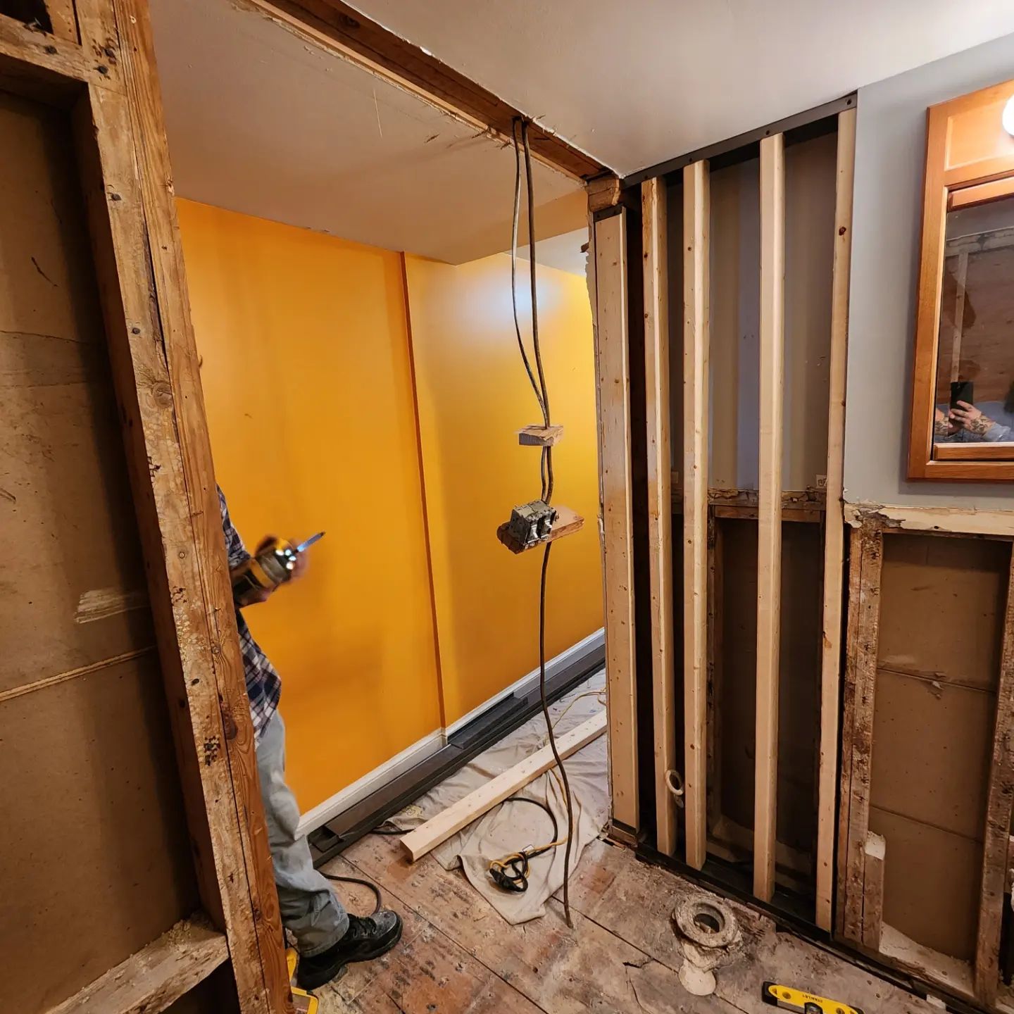 Interior renovation with exposed wall studs, orange insulation, and a worker drilling on the left