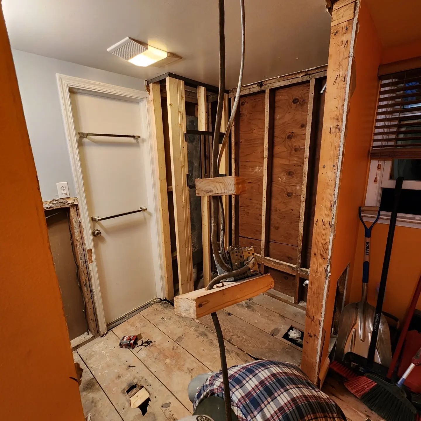 Partially demolished room with exposed wall studs, hanging wires, and debris on the tiled floor