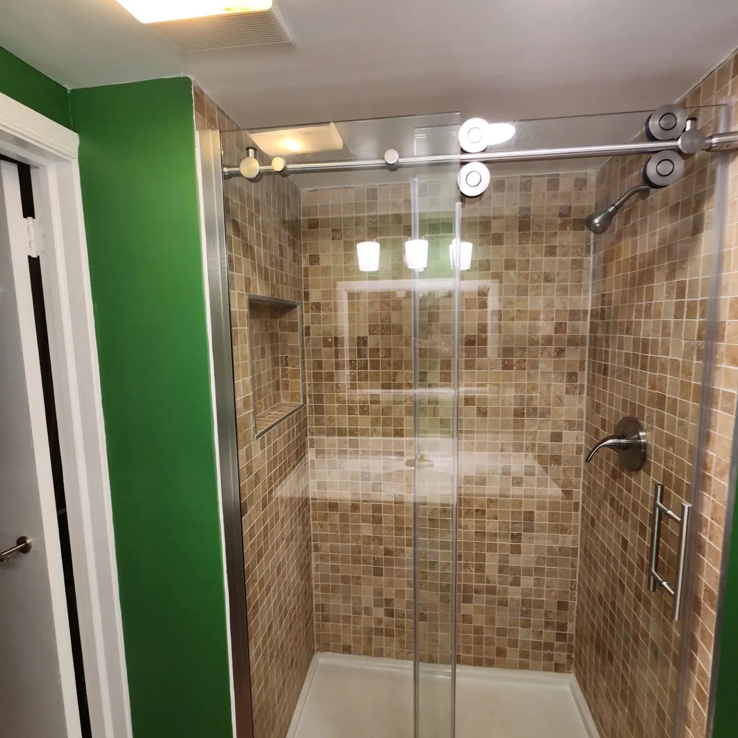 Small tiled shower stall with sliding glass doors and chrome fixtures beside a green wall.