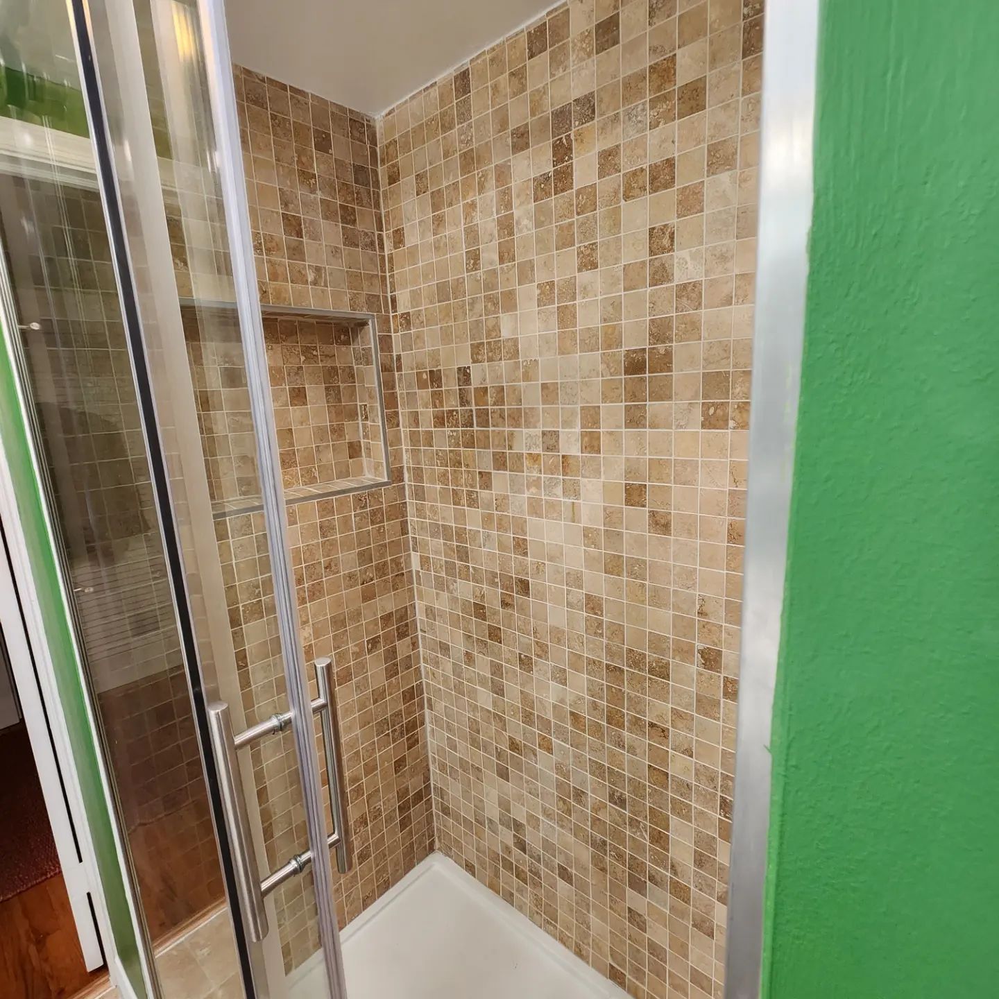 Small tiled shower stall with a glass door and beige mosaic walls.