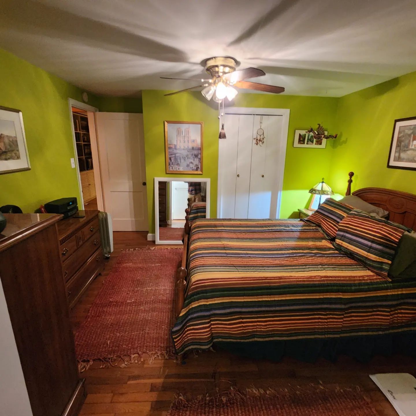 Bright bedroom with lime green walls, striped bedspread, dresser, mirror, and ceiling fan.
