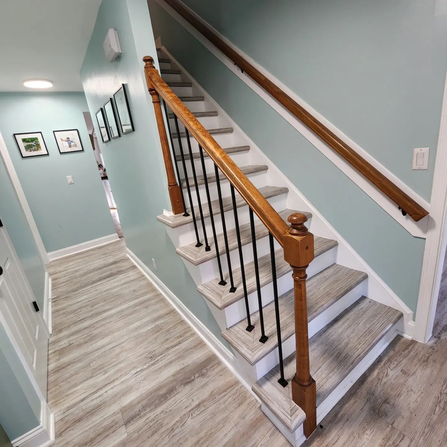 Staircase with wood handrail and white steps in a light blue hallway, next to a wood-look floor.