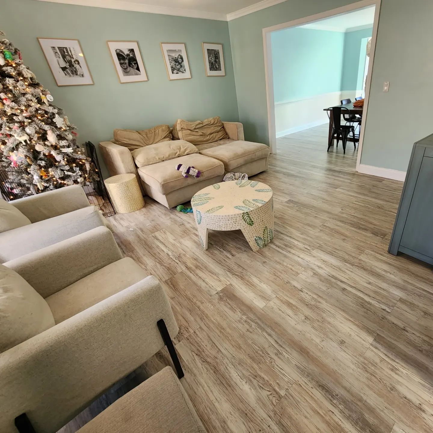 Bright living room with beige sofas, floral coffee table, wood floor, and a lit Christmas tree in the corner