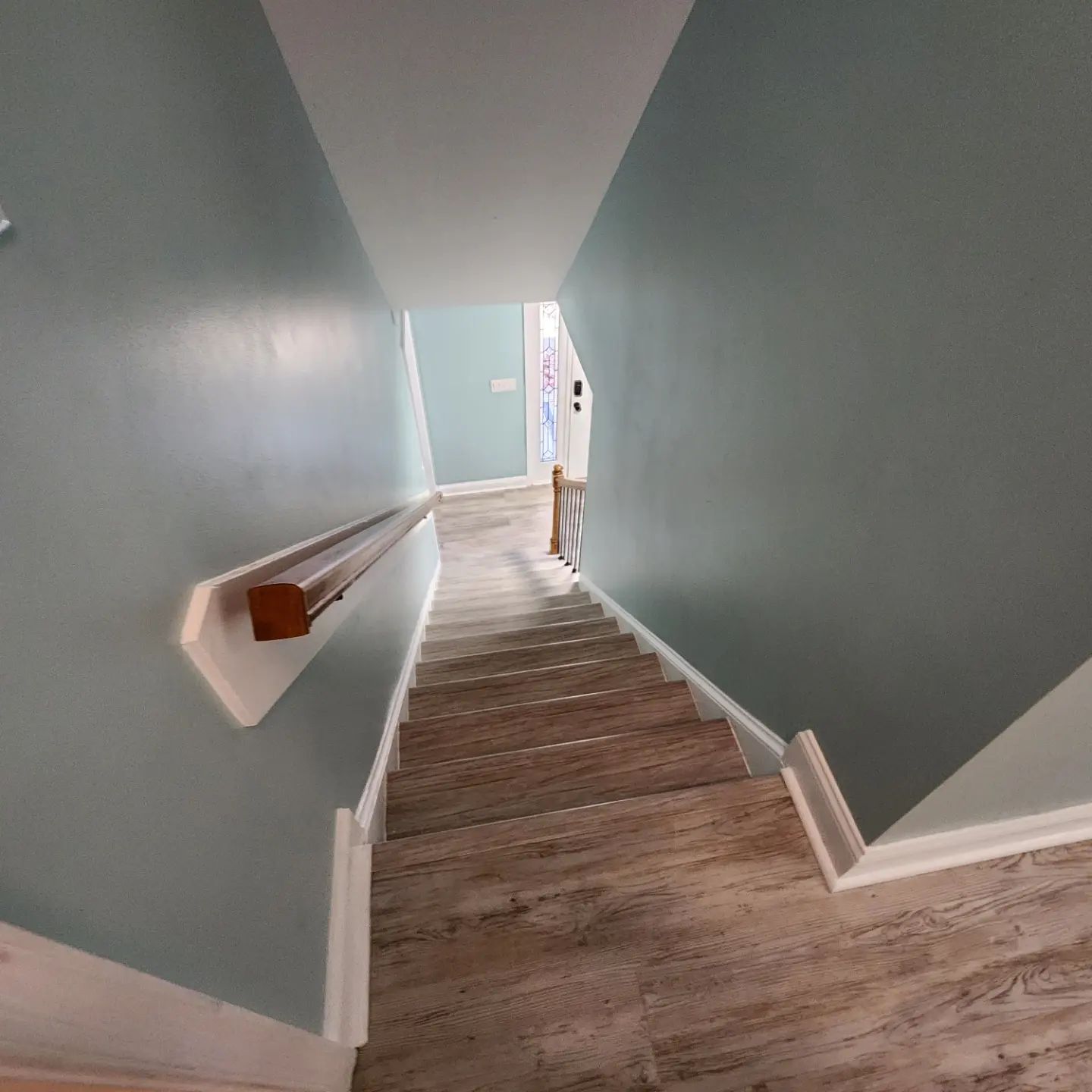 Staircase descending into a light blue entryway with white trim and wood flooring