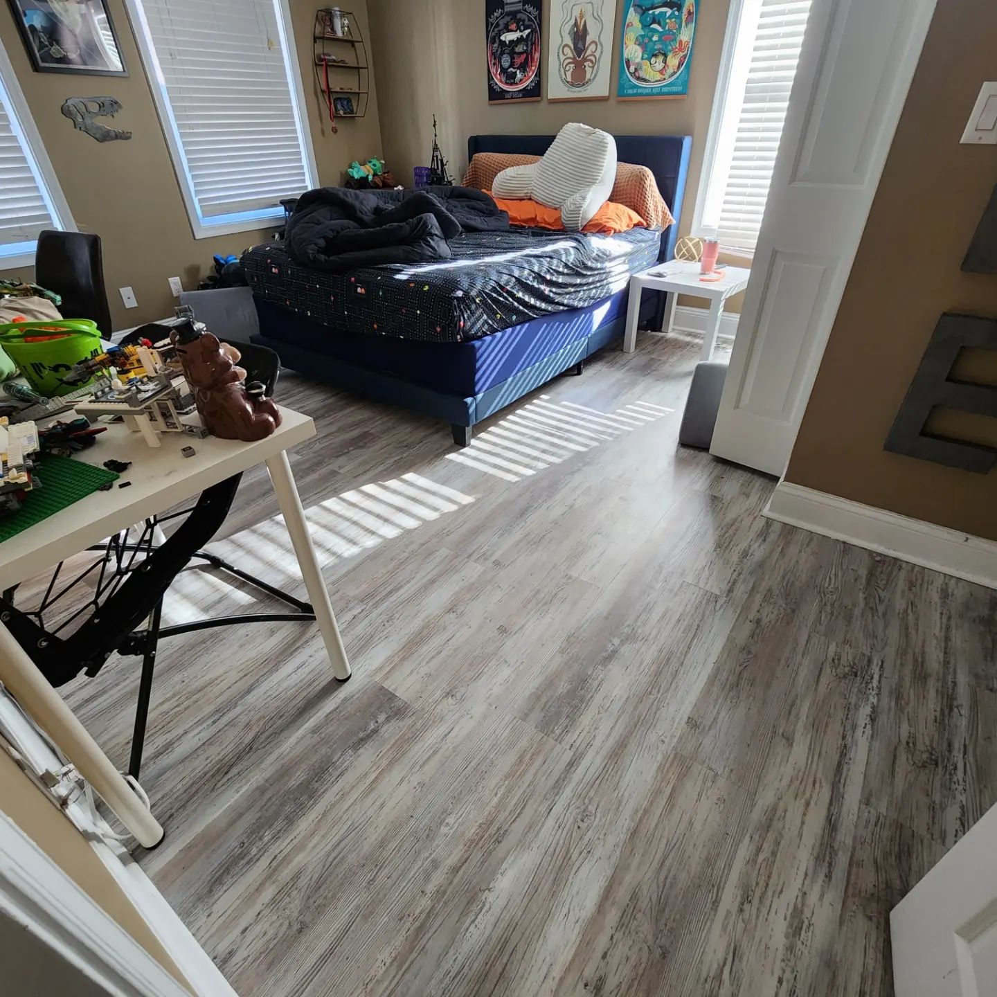 Bedroom with unmade bed, desk, and gray wood-look flooring in daylight