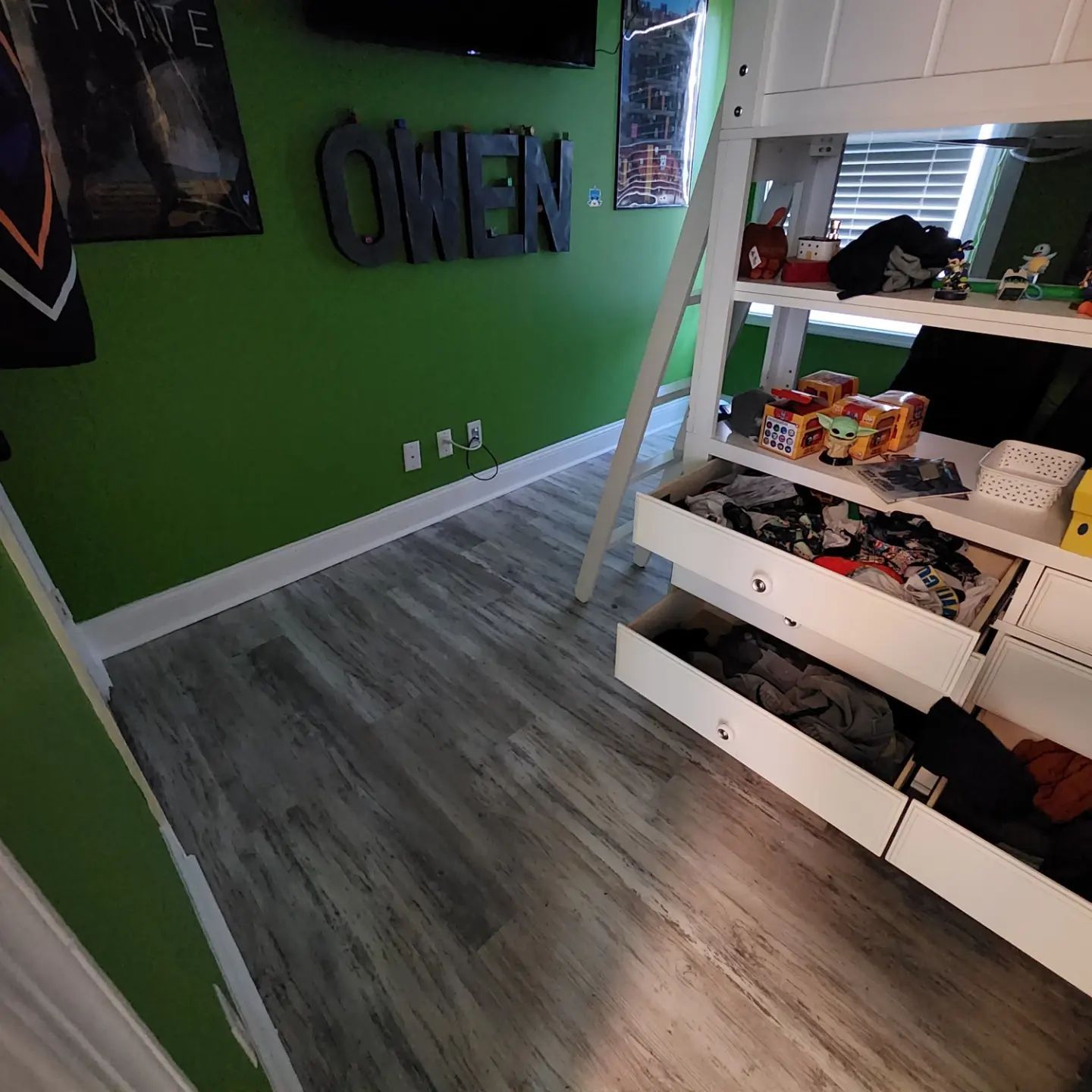Small bedroom with green wall, gray wood floor, and a white bunk bed with storage drawers.