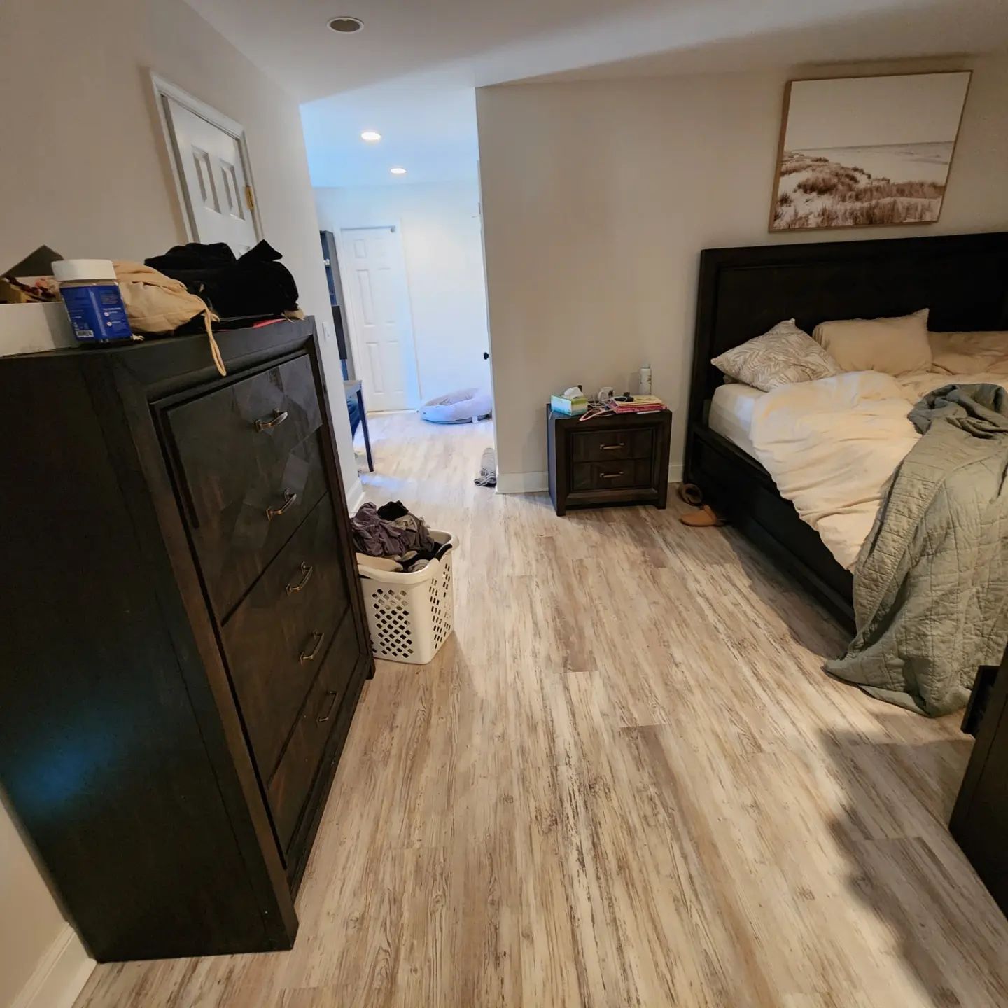 Bedroom with bed, dresser, and laundry basket in a narrow hallway view