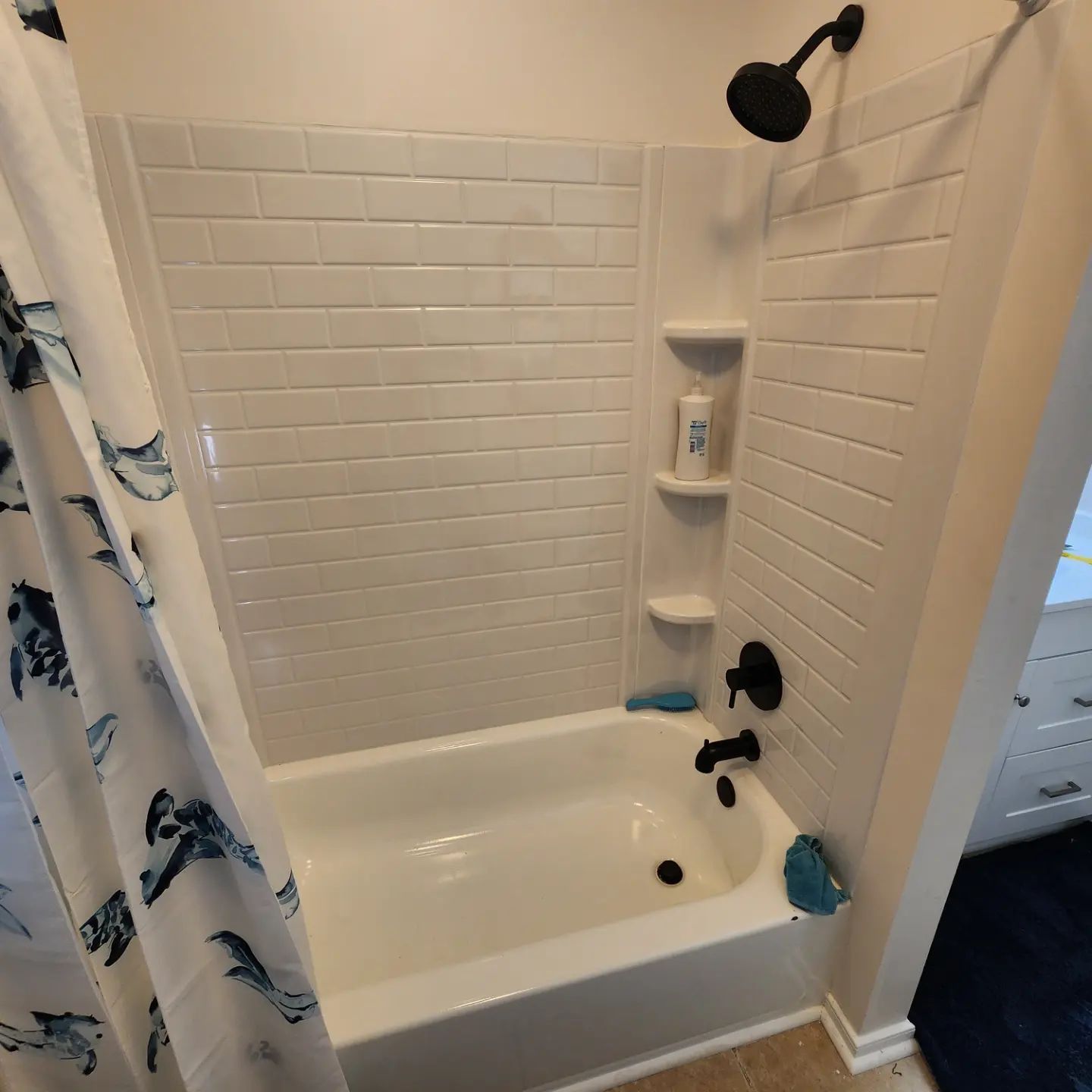 White bathtub and shower with white tile walls, black fixtures, and a blue shark shower curtain