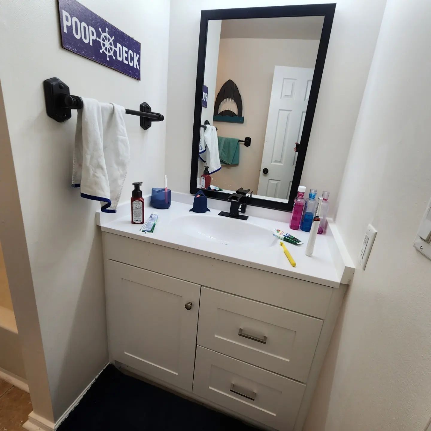Bathroom vanity with mirror, white cabinets, and toiletries on the counter.