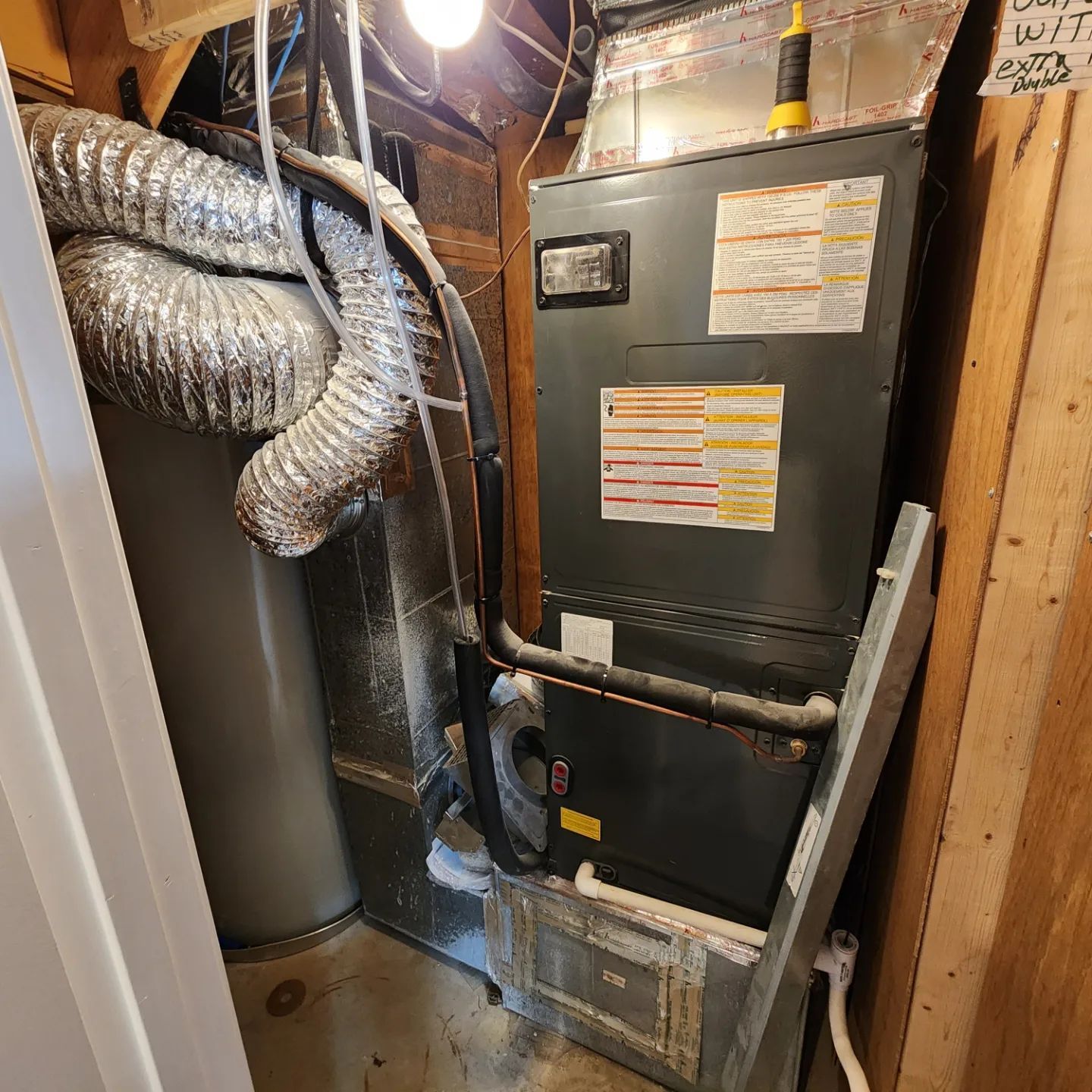 Furnace and ductwork in a cramped utility closet with exposed insulation and pipes.
