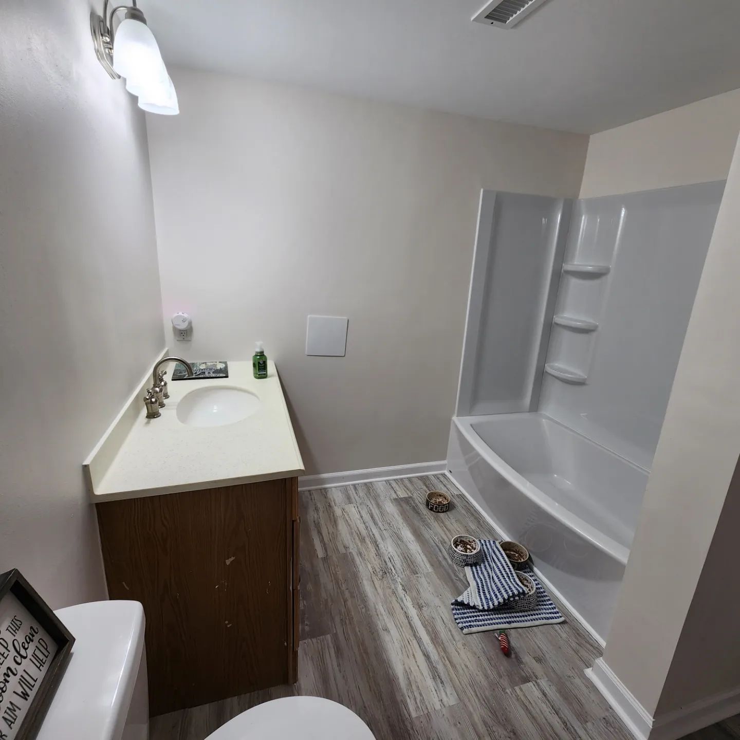 Small bathroom with vanity sink and a white tub/shower; cleaning supplies lie on the floor.