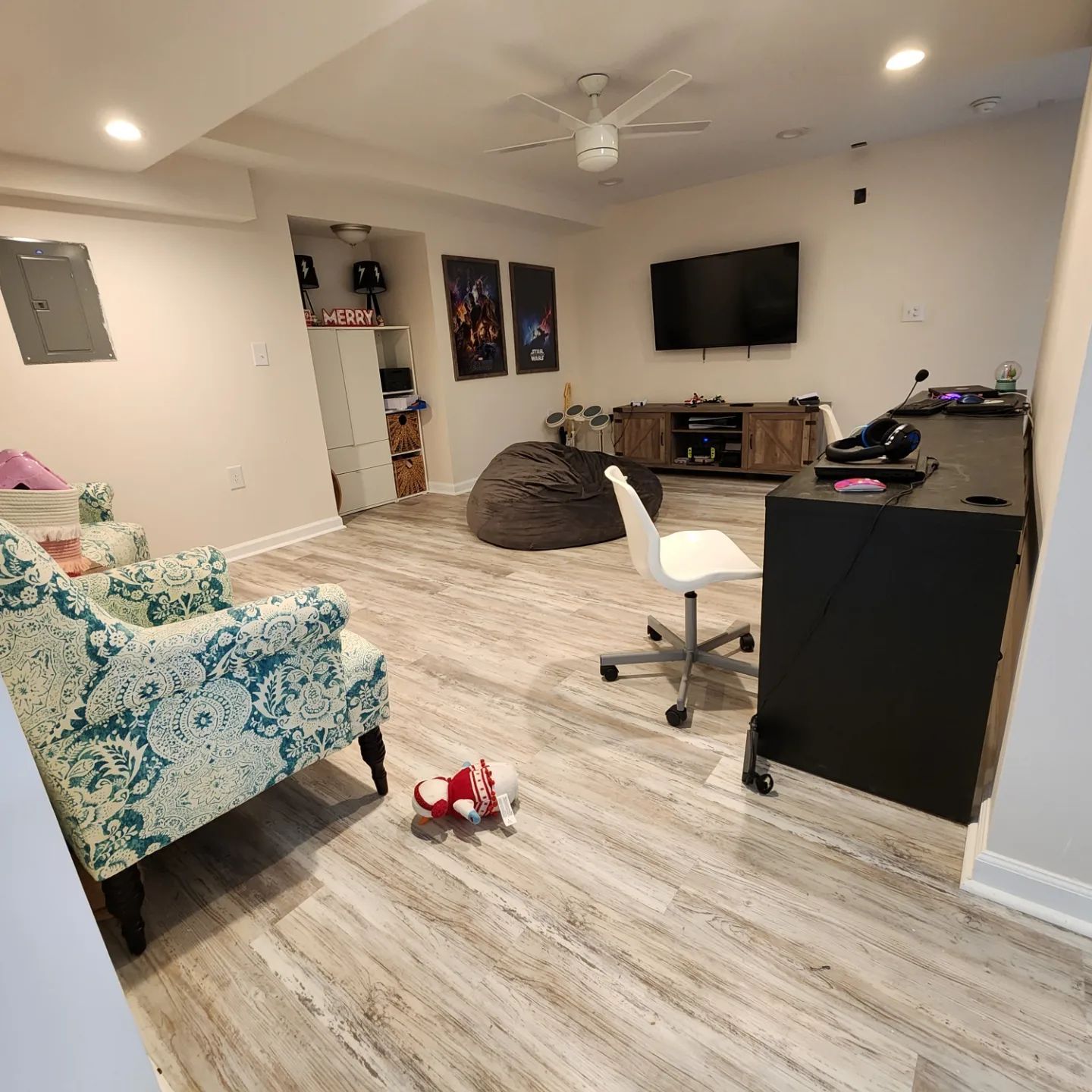 Living room with floral armchair, TV, desk, beanbag, and scattered toys on light wood floor