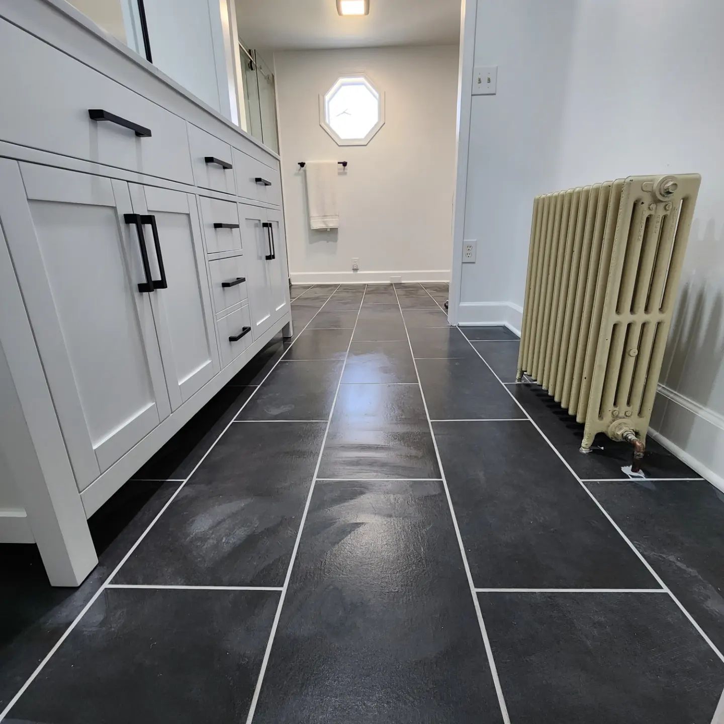 Modern bathroom with dark tile floor, white vanity, and a beige radiator