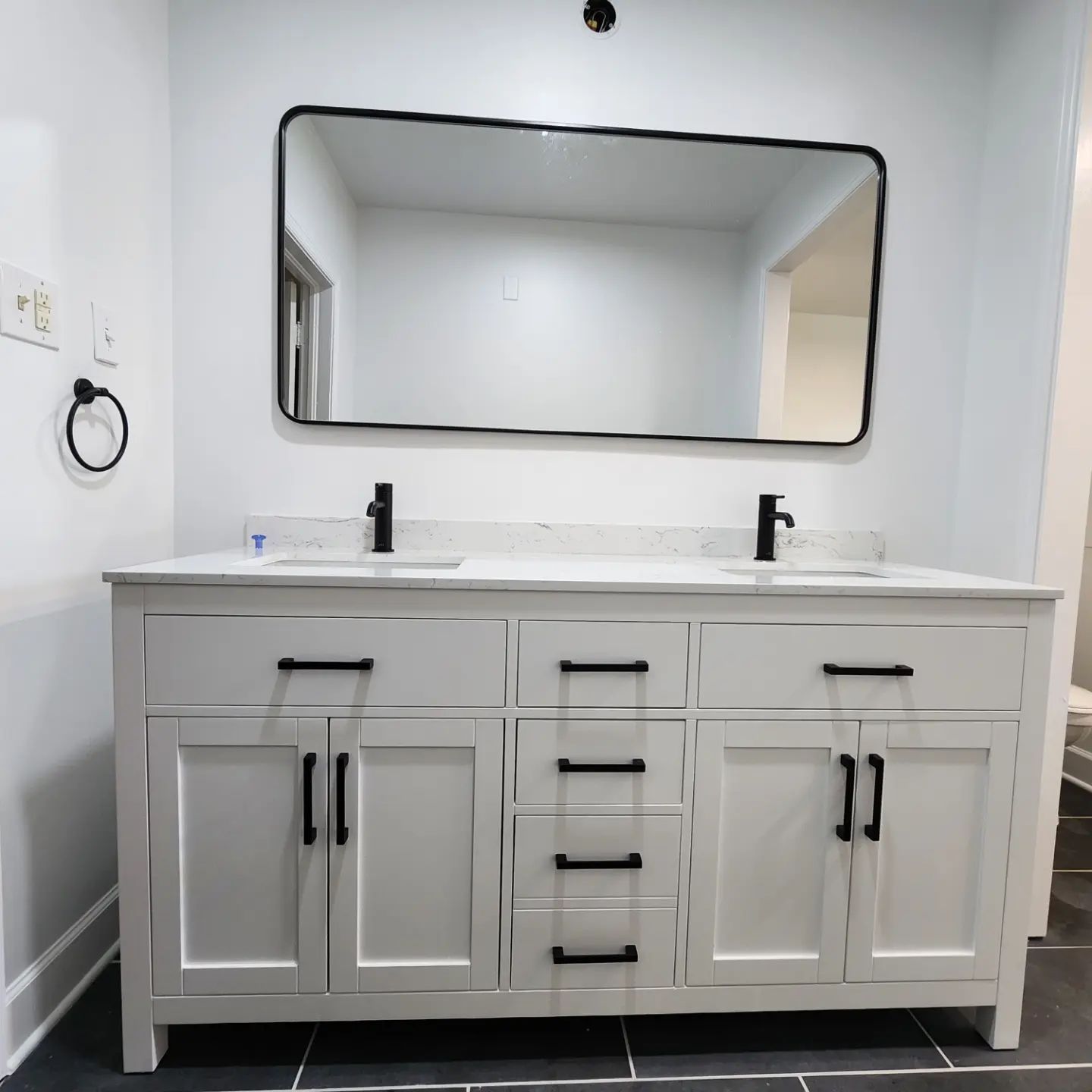 White double-sink bathroom vanity with mirror and black fixtures in a bright room