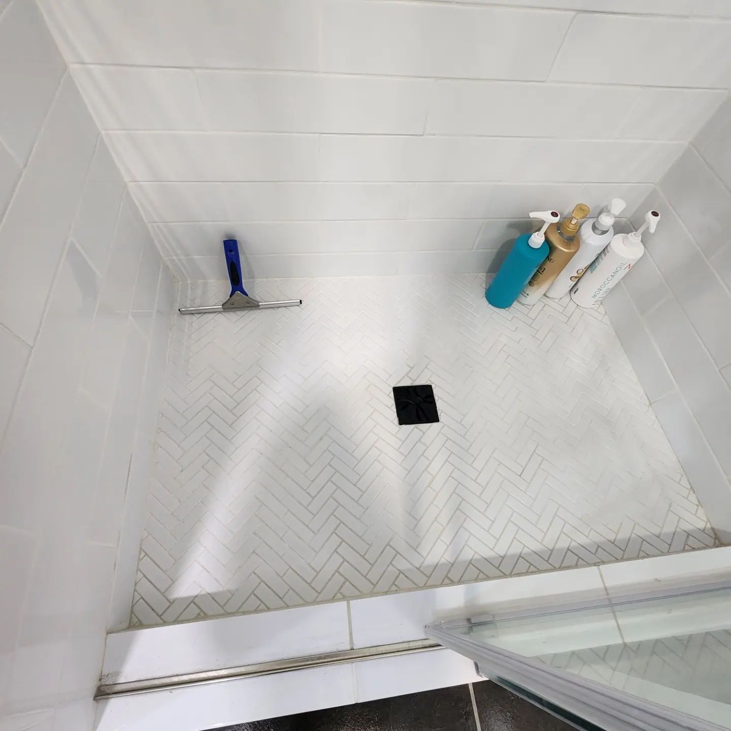 White tiled shower with herringbone floor, black drain, and blue and gold shower fixtures.
