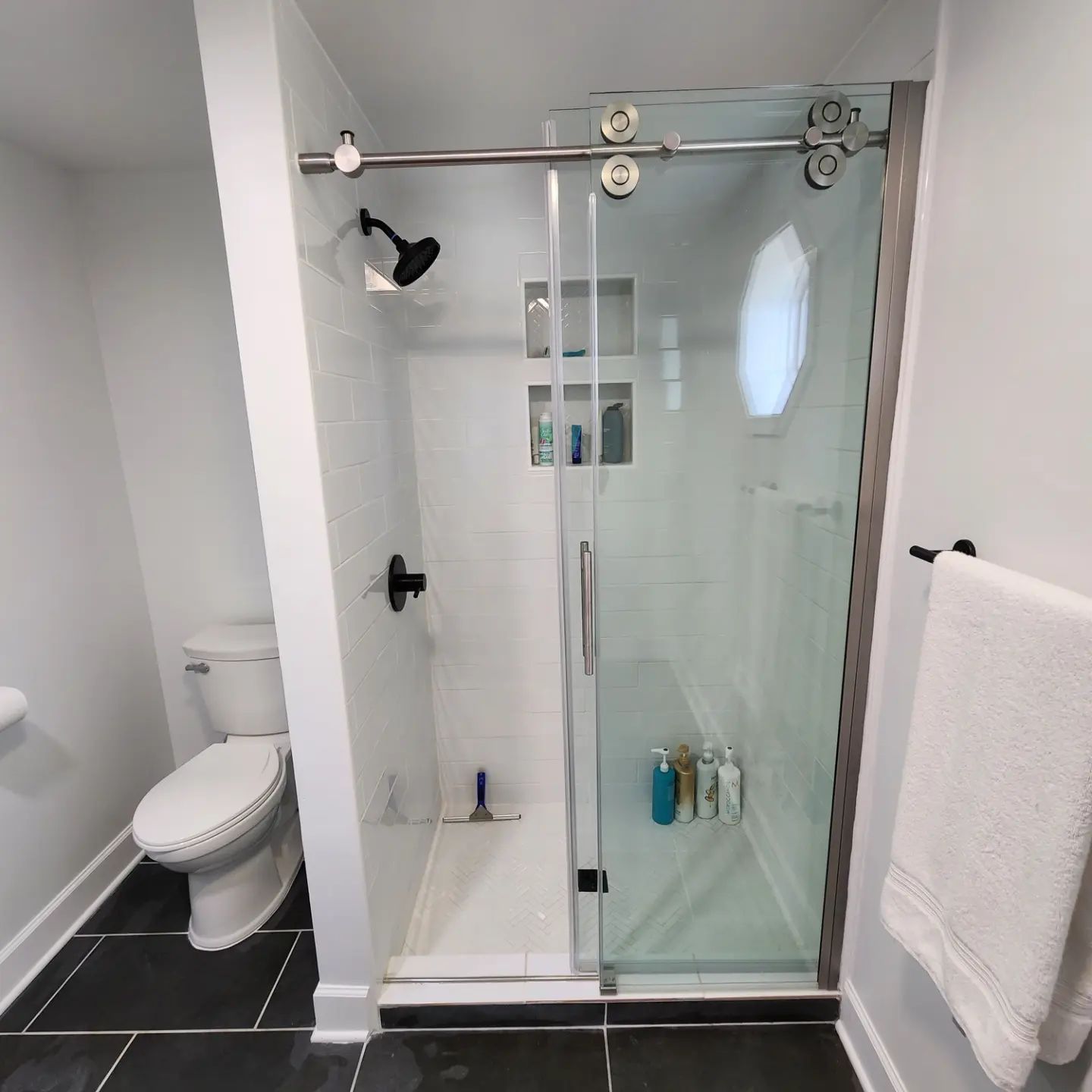 Modern bathroom with a glass shower, toilet, black tile floor, and white towel on a wall rack