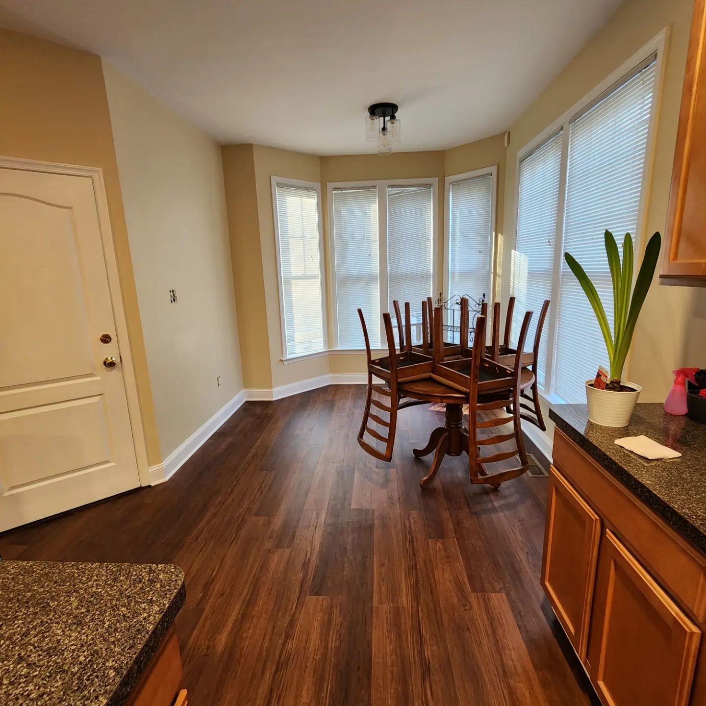 Dining room with dark wood floors, a table with chairs upside down on it, bay windows, and a wooden cabinet.