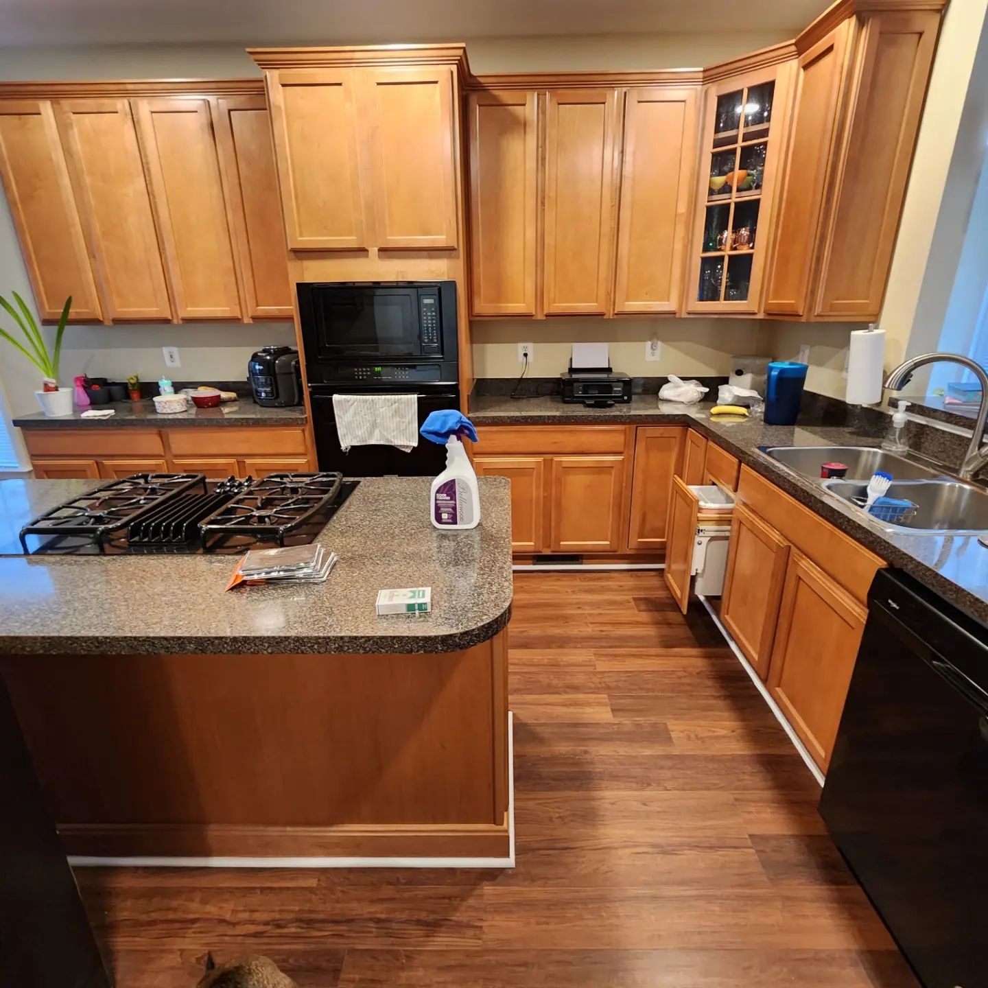 Modern kitchen with wooden cabinets, granite island, black appliances, and a stainless-steel sink.