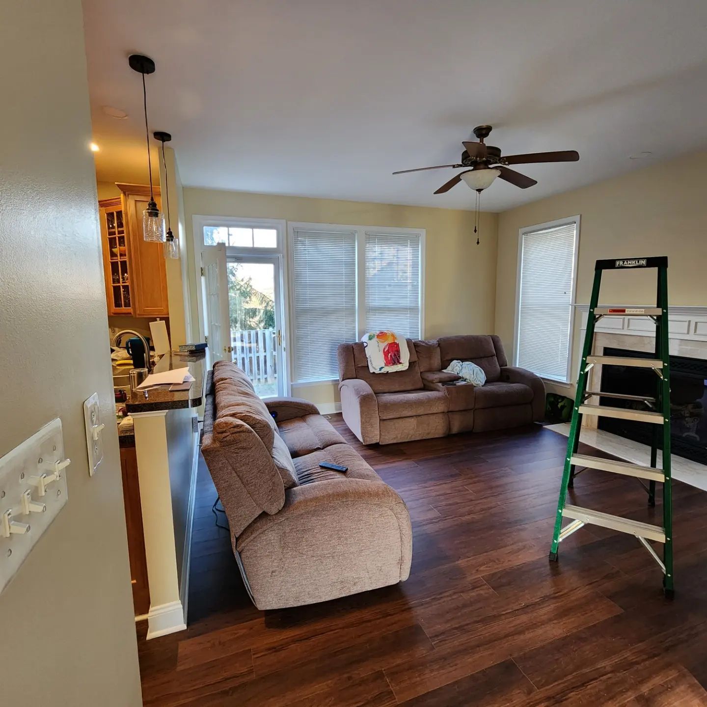 Living room with brown sofa, loveseat, ceiling fan, and a green ladder near sliding glass doors.