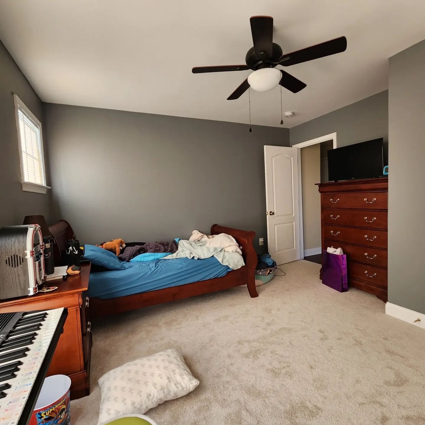 Bedroom with gray walls, bed, dresser, ceiling fan, and a keyboard in the foreground.