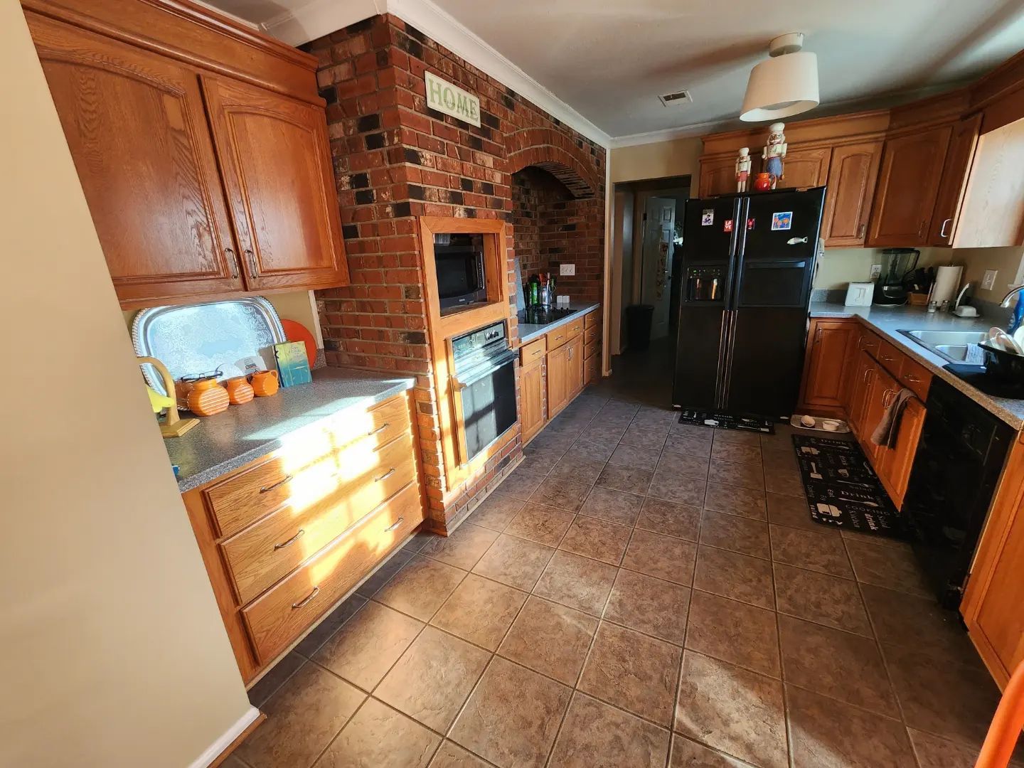 Kitchen interior with brick accent wall, wood cabinets, black appliances, and tiled floor