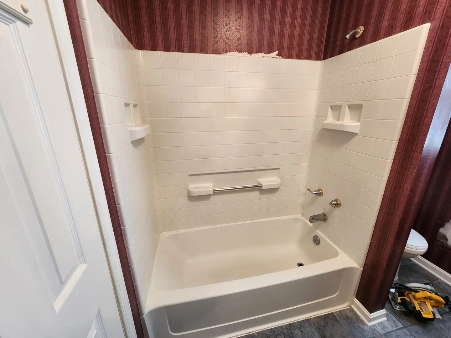 Small white bathtub and tiled shower surround with grab bars in a bathroom
