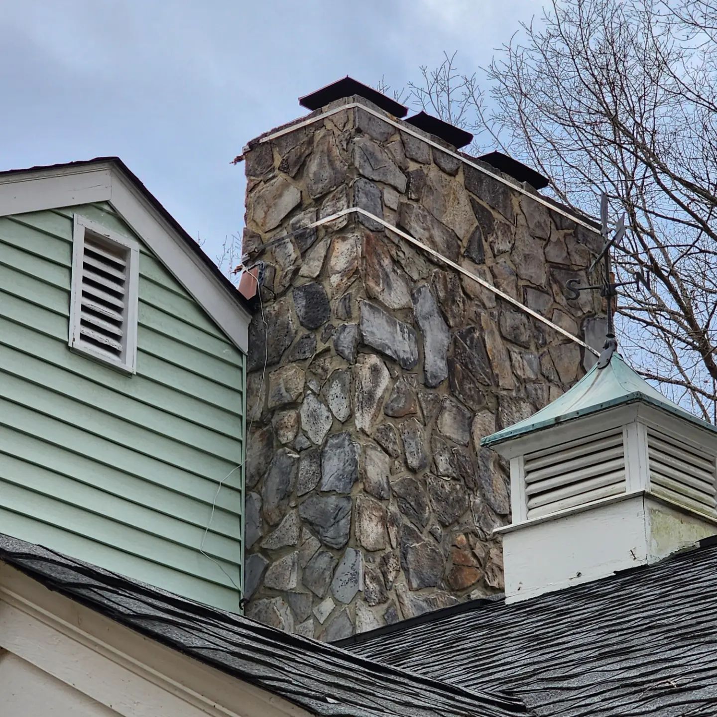Stone chimney beside mint-green and white house roofs under a cloudy sky