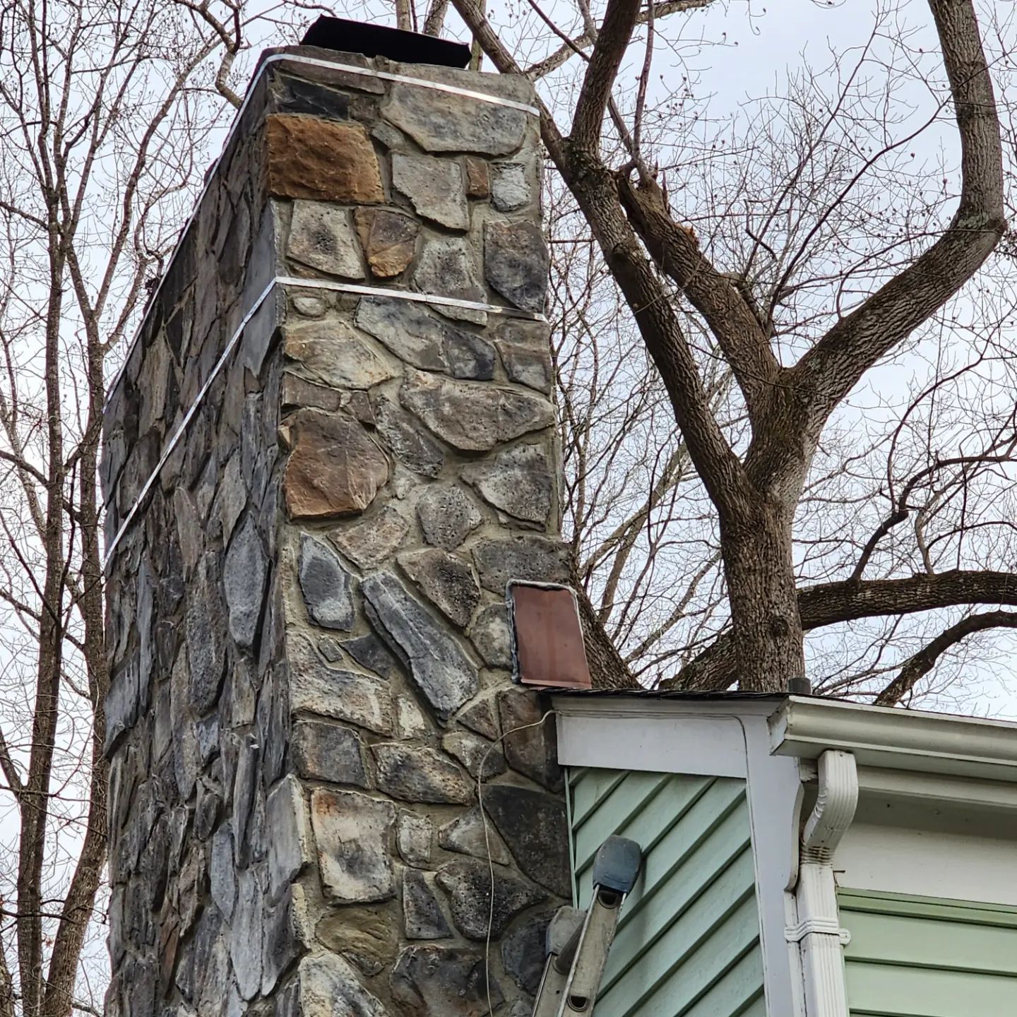 Stone chimney beside a white house under bare winter trees
