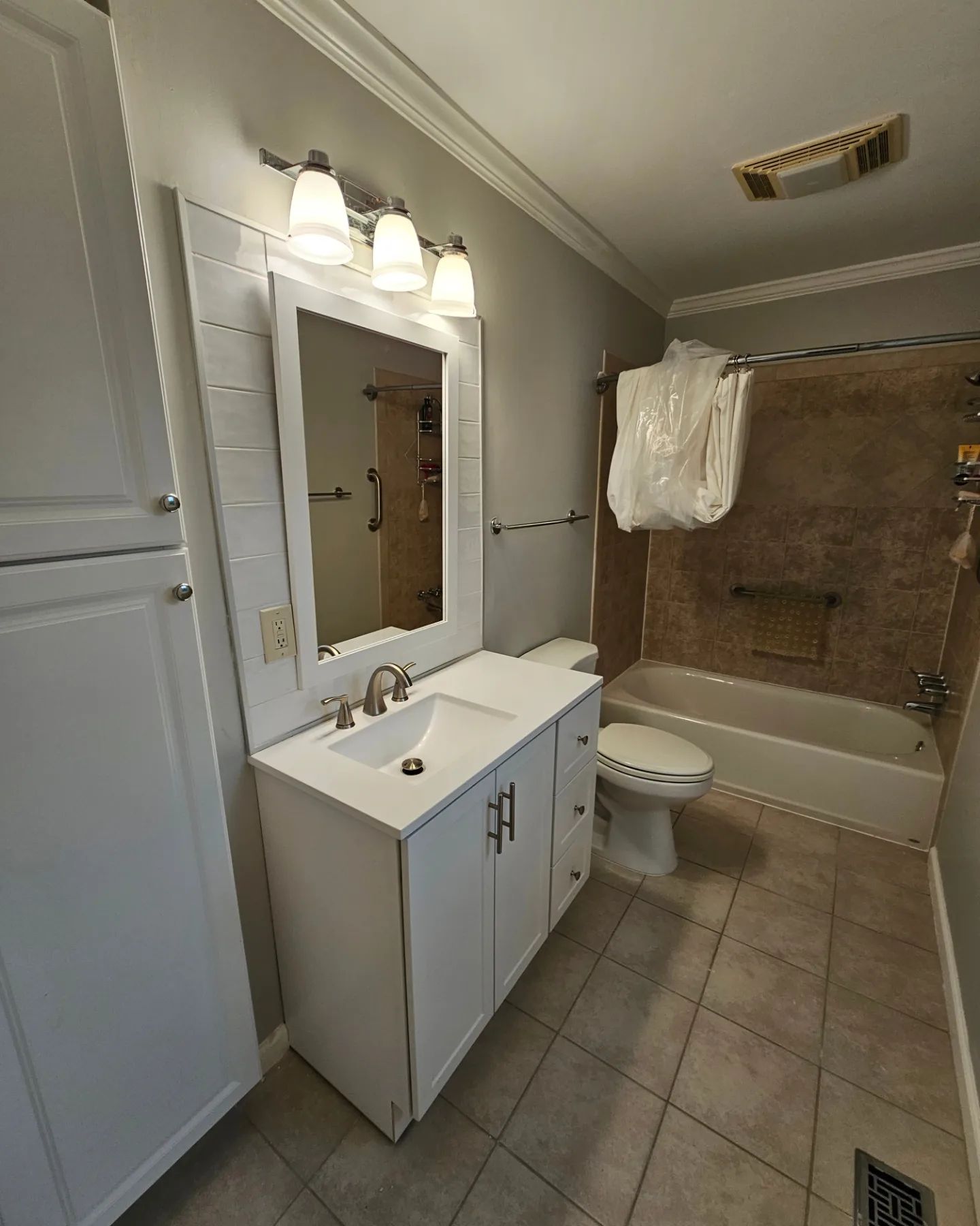 Bathroom with white vanity, mirror, toilet, and bathtub with shower curtain in a tiled room.