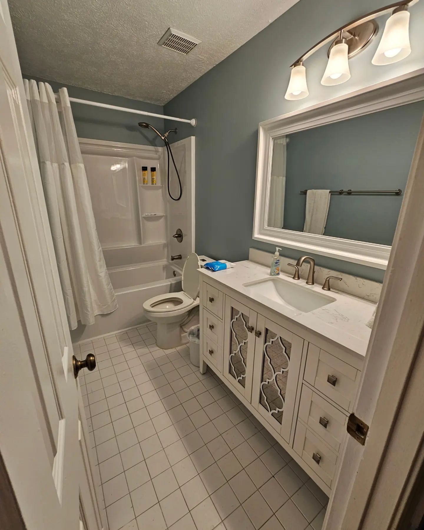 Bright bathroom with white vanity, large mirror, shower curtain, and tiled floor