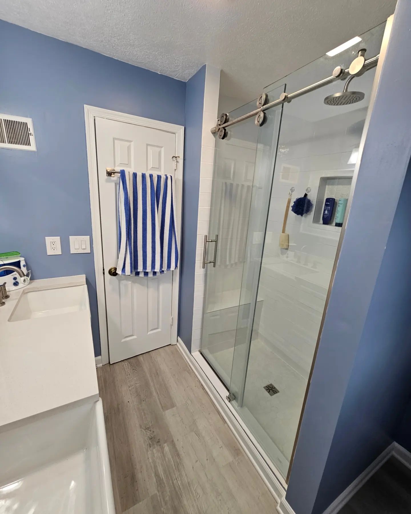 Blue bathroom with white vanity, glass shower, and striped towel hanging on the door