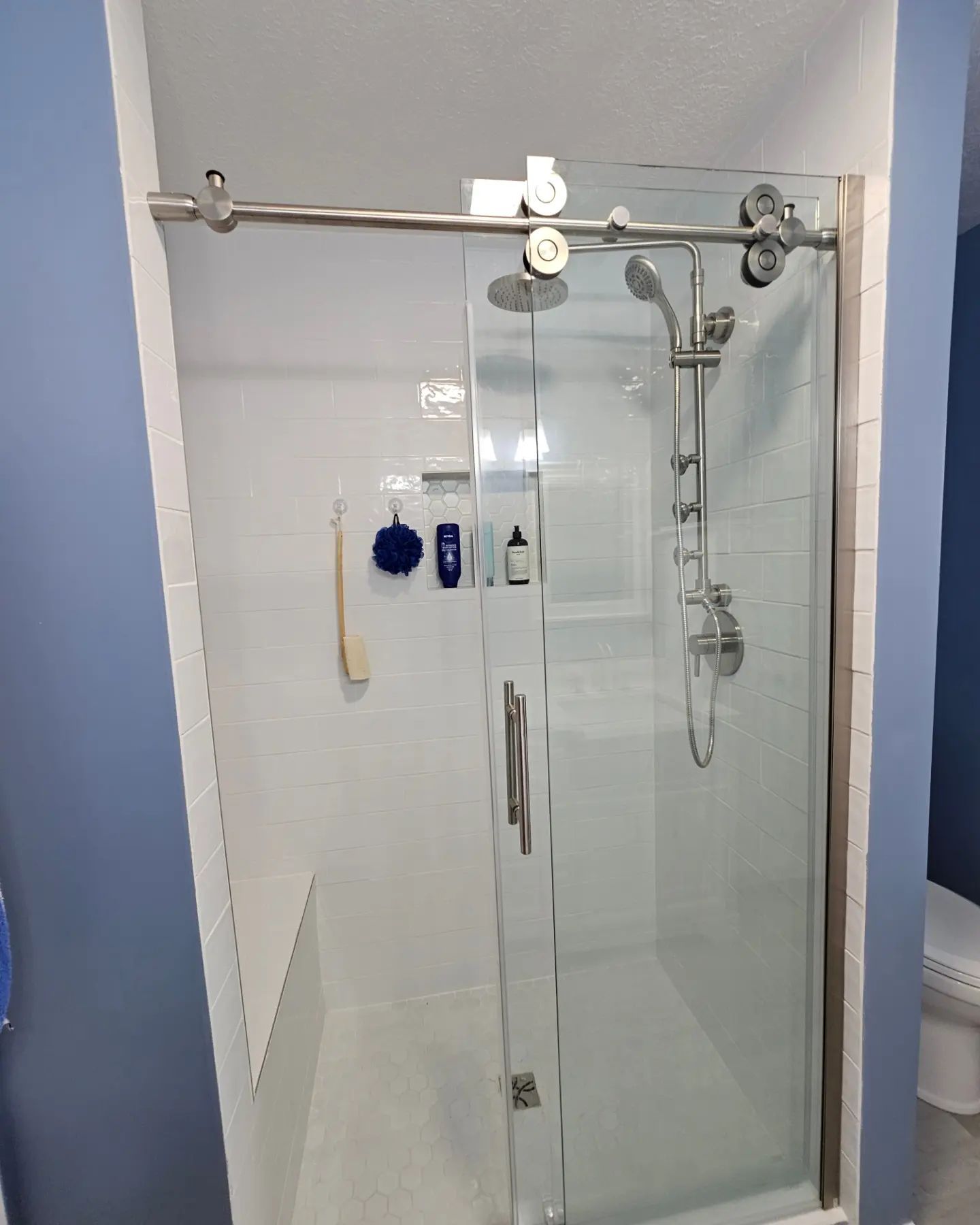 Glass shower enclosure with chrome fixtures and a sliding door in a white-tiled bathroom