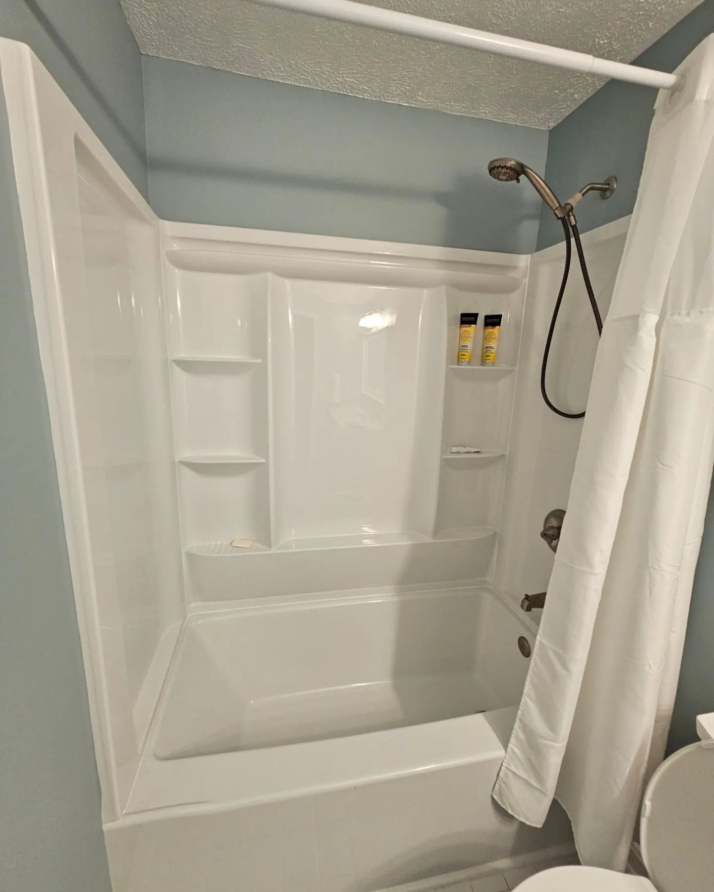 White shower/tub combo with built-in shelves, chrome showerhead, and a hanging white curtain in a bathroom