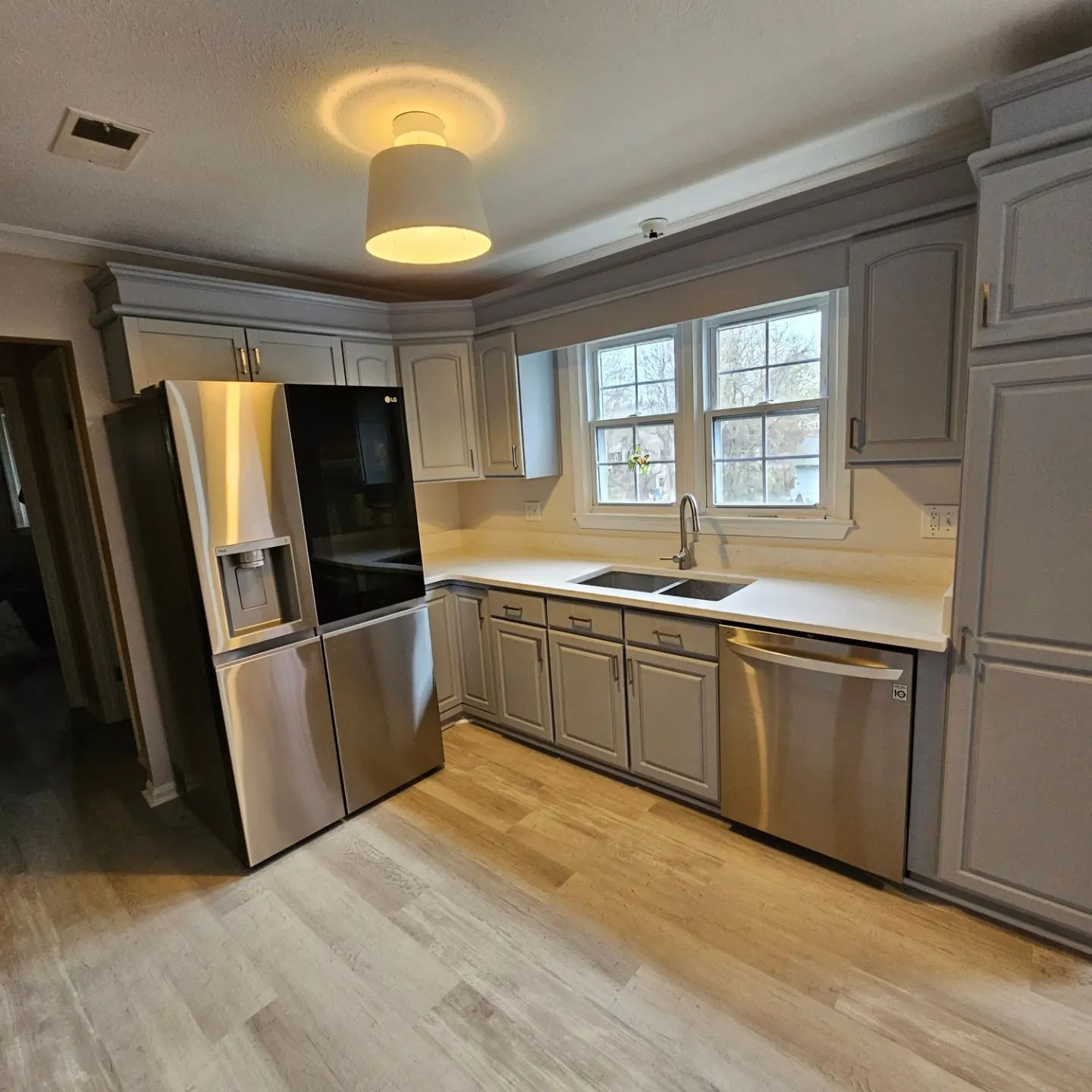 Modern kitchen with stainless steel fridge and dishwasher, gray cabinets, white counters, and wood flooring