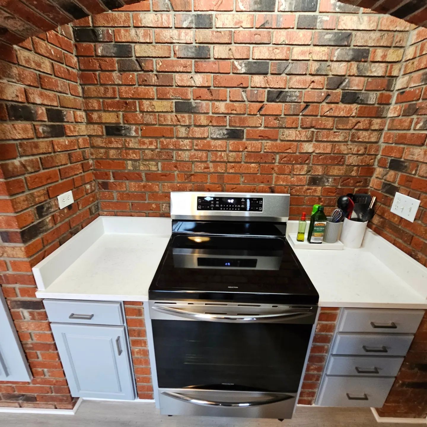 Kitchen stove centered between white cabinets against a red brick backsplash and walls