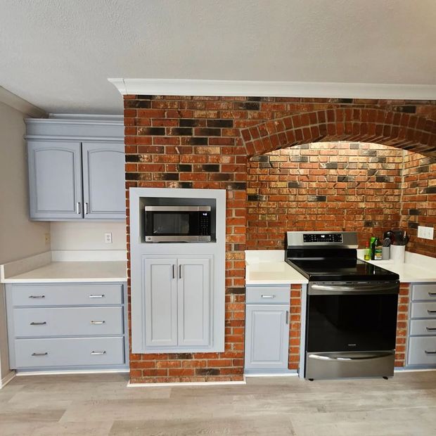 Kitchen with red brick accent wall, gray cabinets, built-in microwave, and black stove with stainless-steel oven
